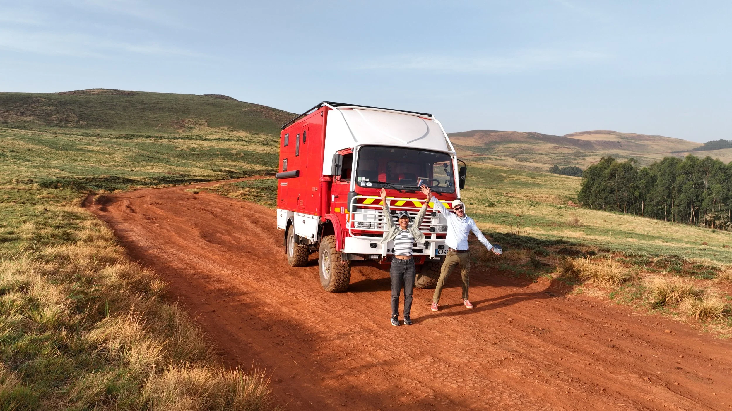 Justin et Bee devant le RedTruck sur une piste de latérite au Nigeria, heureux de débuter leur aventure en Afrique centrale dans un décor magnifique.