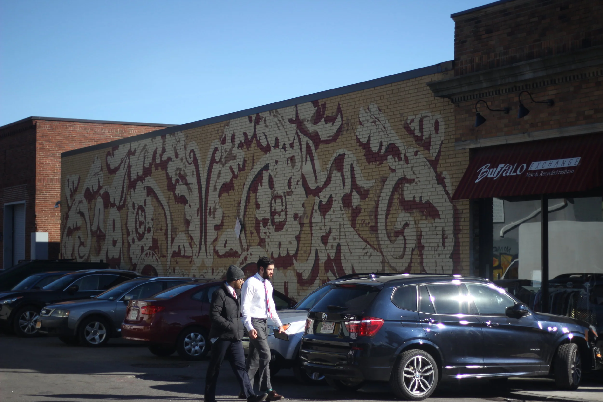 Two gentleman walk from their car past a mural. Businesses covered in art seems to have become a trend over the years attracting college age students to live there. (Artist Unknown.)