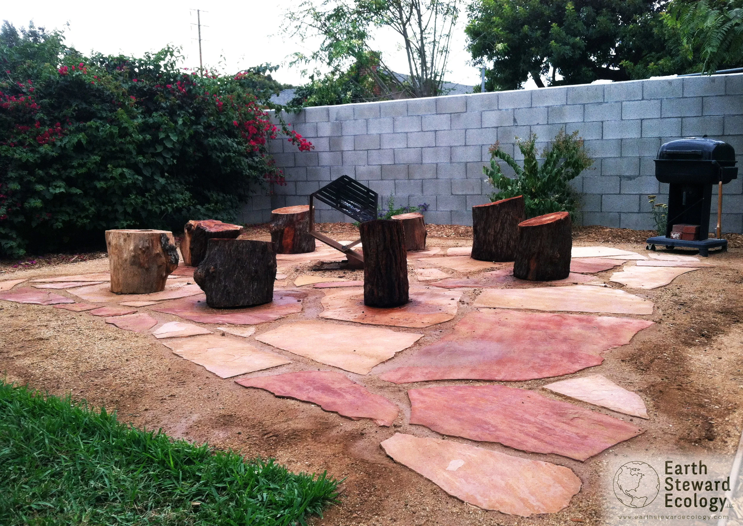 large pieces of flagstone create this wonderful backyard gathering space with tree stump seating surrounding a fire.