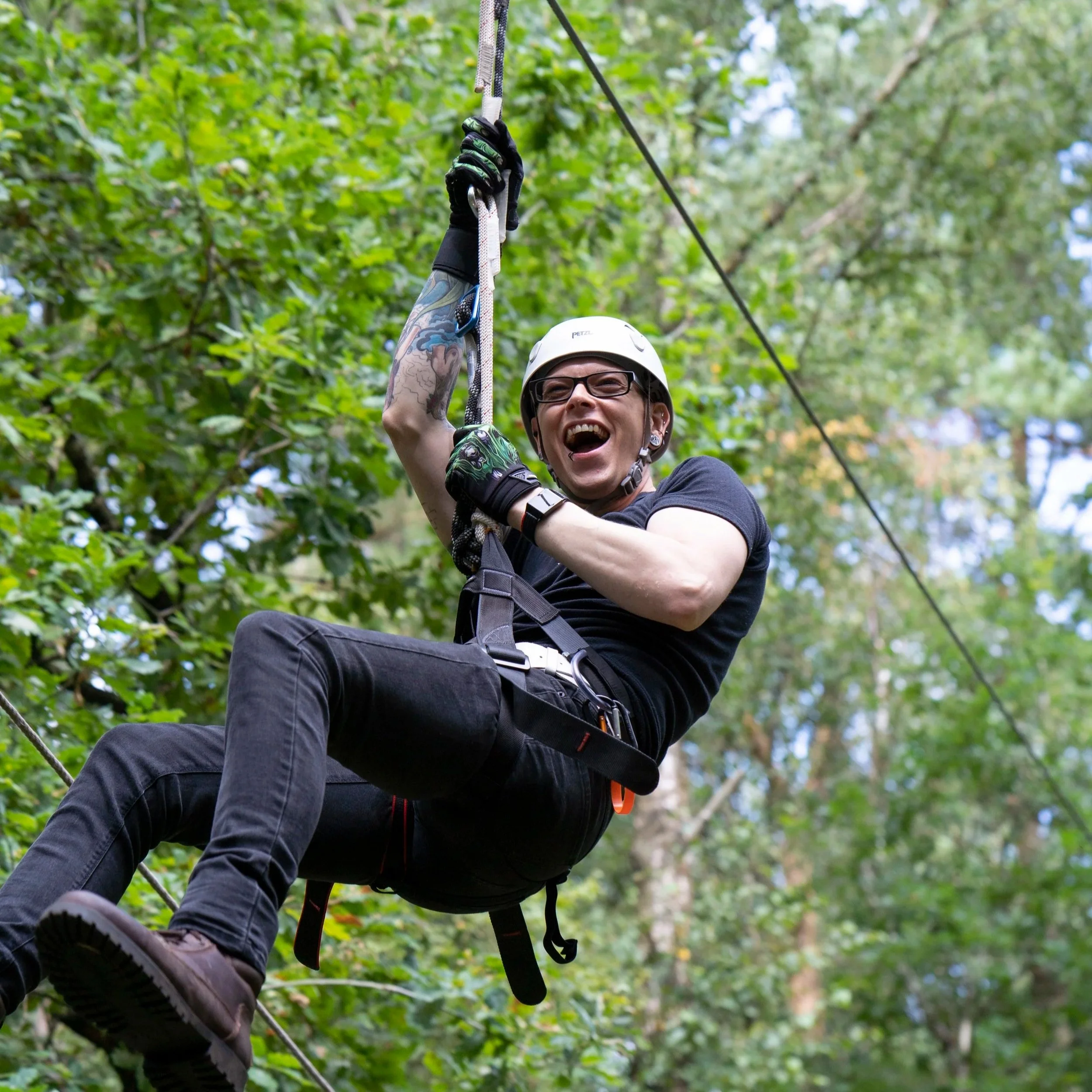 A person wearing a helmet and glasses is mountain biking on a trail in a forest, holding onto a cable or rope with a joyful expression.