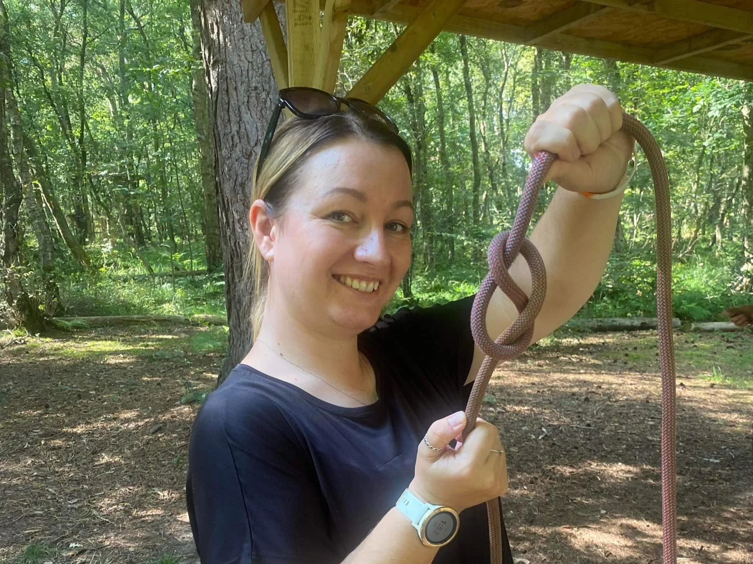 A woman smiling in a forested area holding climbing rope.