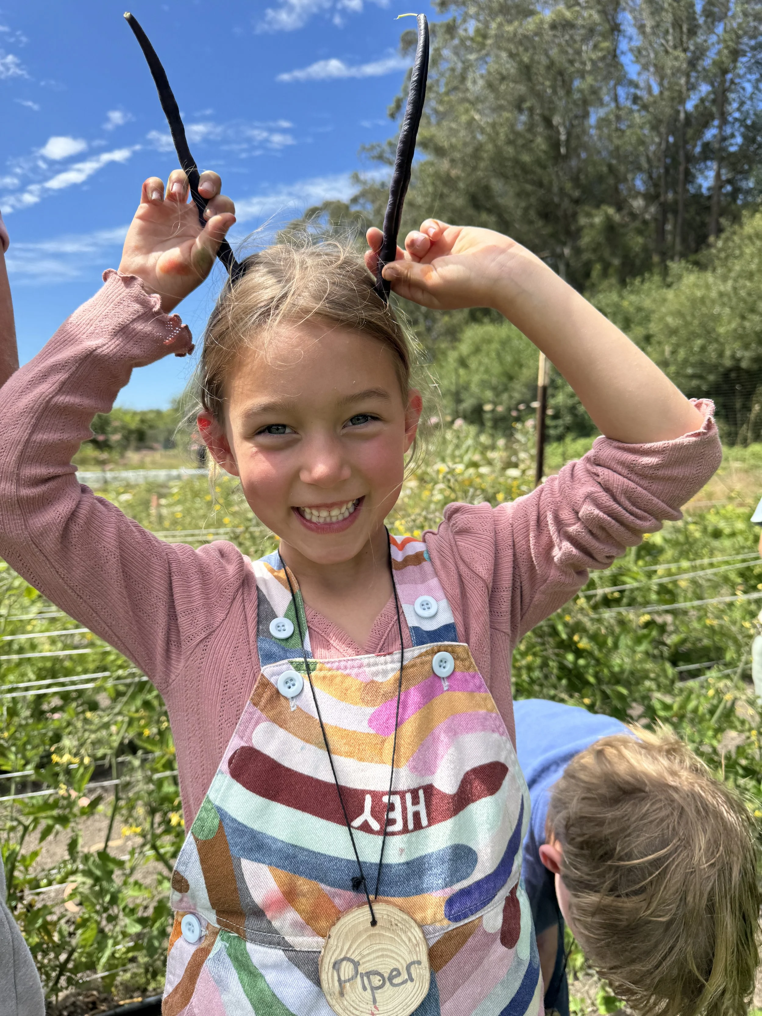 Child holding purple beans up to her head as antennae