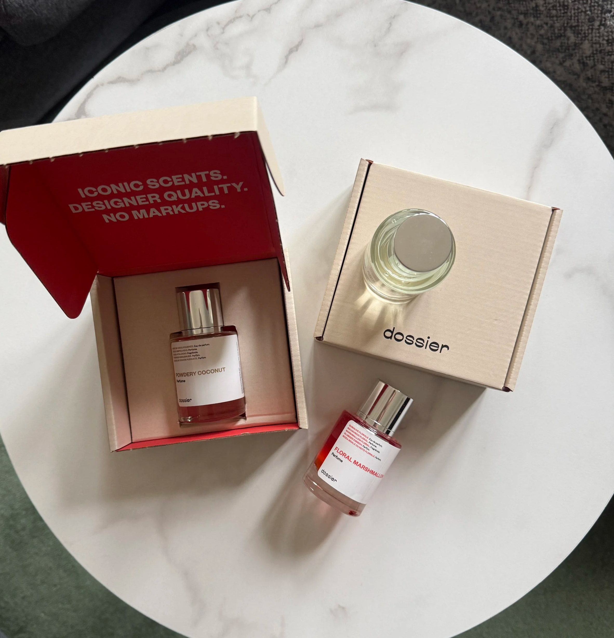 Photo of 3 Dossier Perfumes, "Powdery Coconut", "Floral Marshmallow" and "Ambery Saffron" and 2 boxes pictured on a white marble table