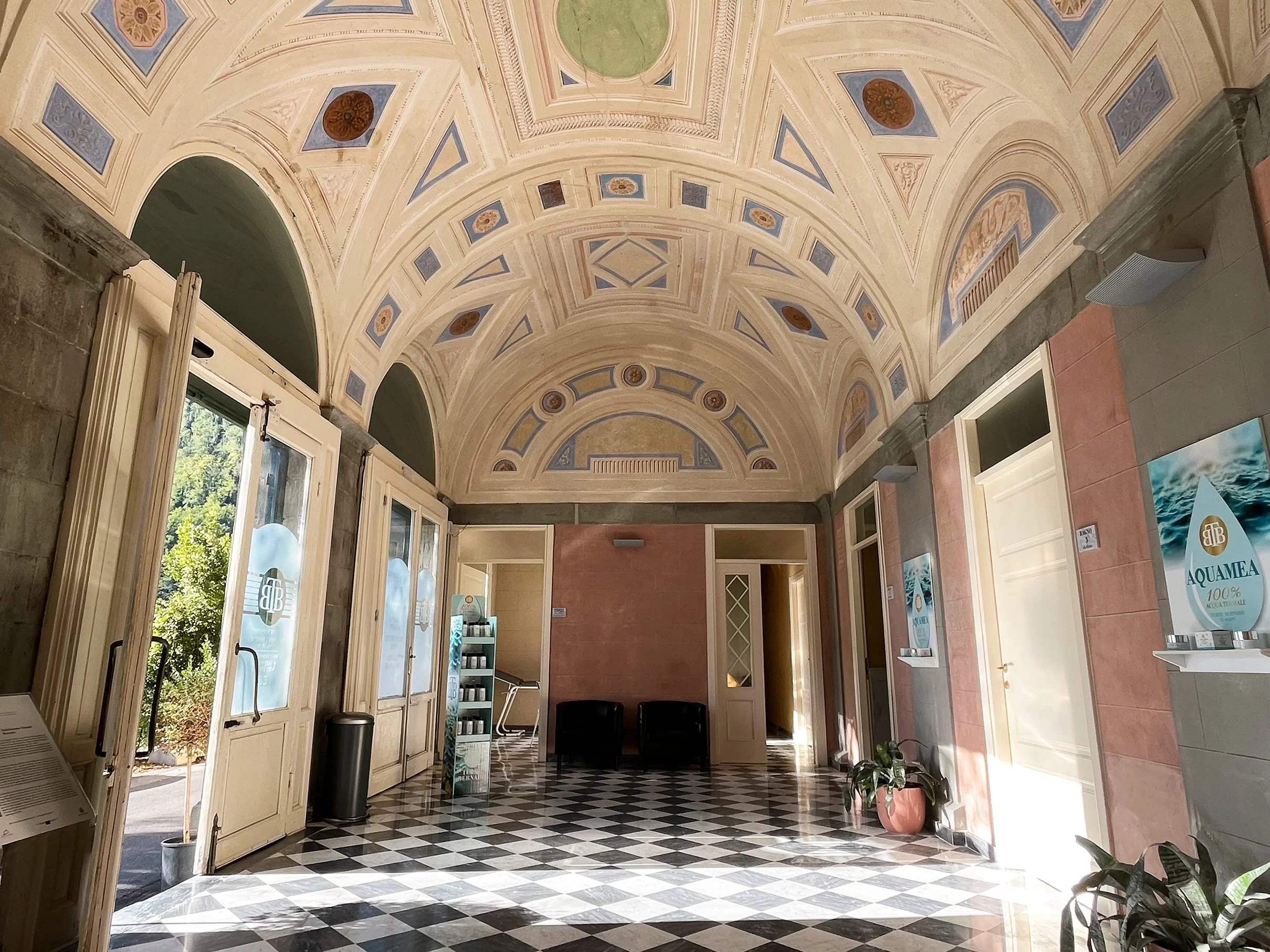 The spa's reception, with black and white floor tiles, soft pink walls, and an arched ceiling with some simple blue frescoes.