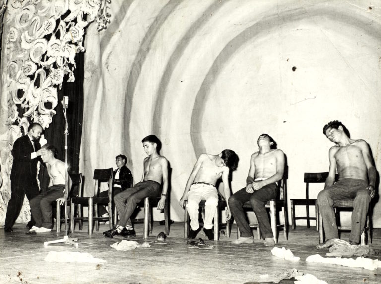 A hypnotist entrances several young men onstage, mid-20th century