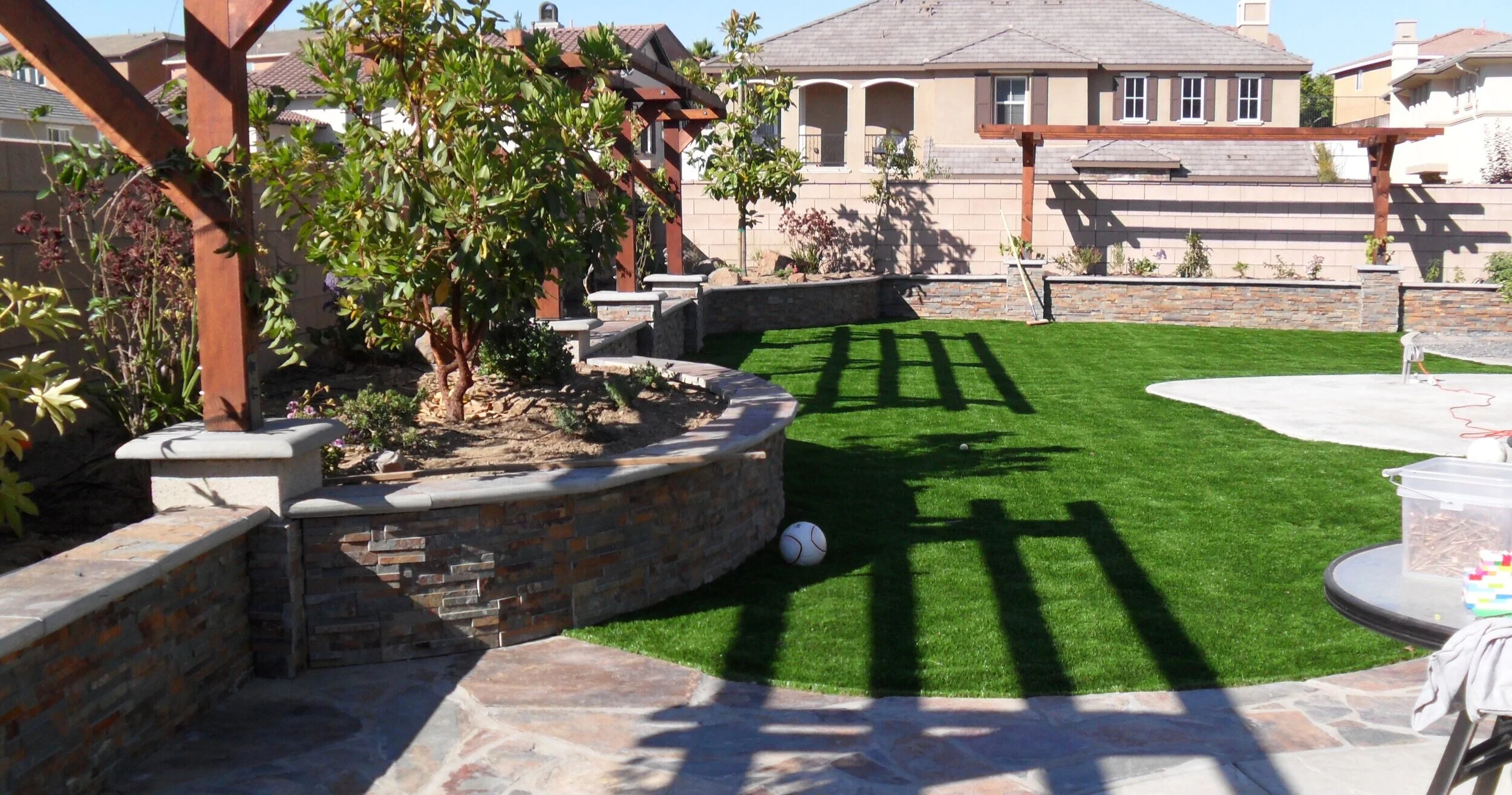 Backyard with a manicured lawn, brick and stone garden beds, trees, and patio furniture.