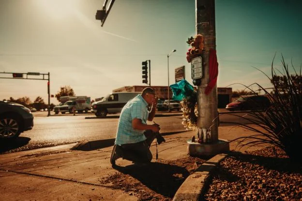 (Megan Aguilar / New Mexico News Port) Albuquerque Journal photographer Roberto Rosales pays his respects before photographing a small shrine created for Joel Suina, the 6-year-old victim of a police officer involved car crash. The photo was for an …