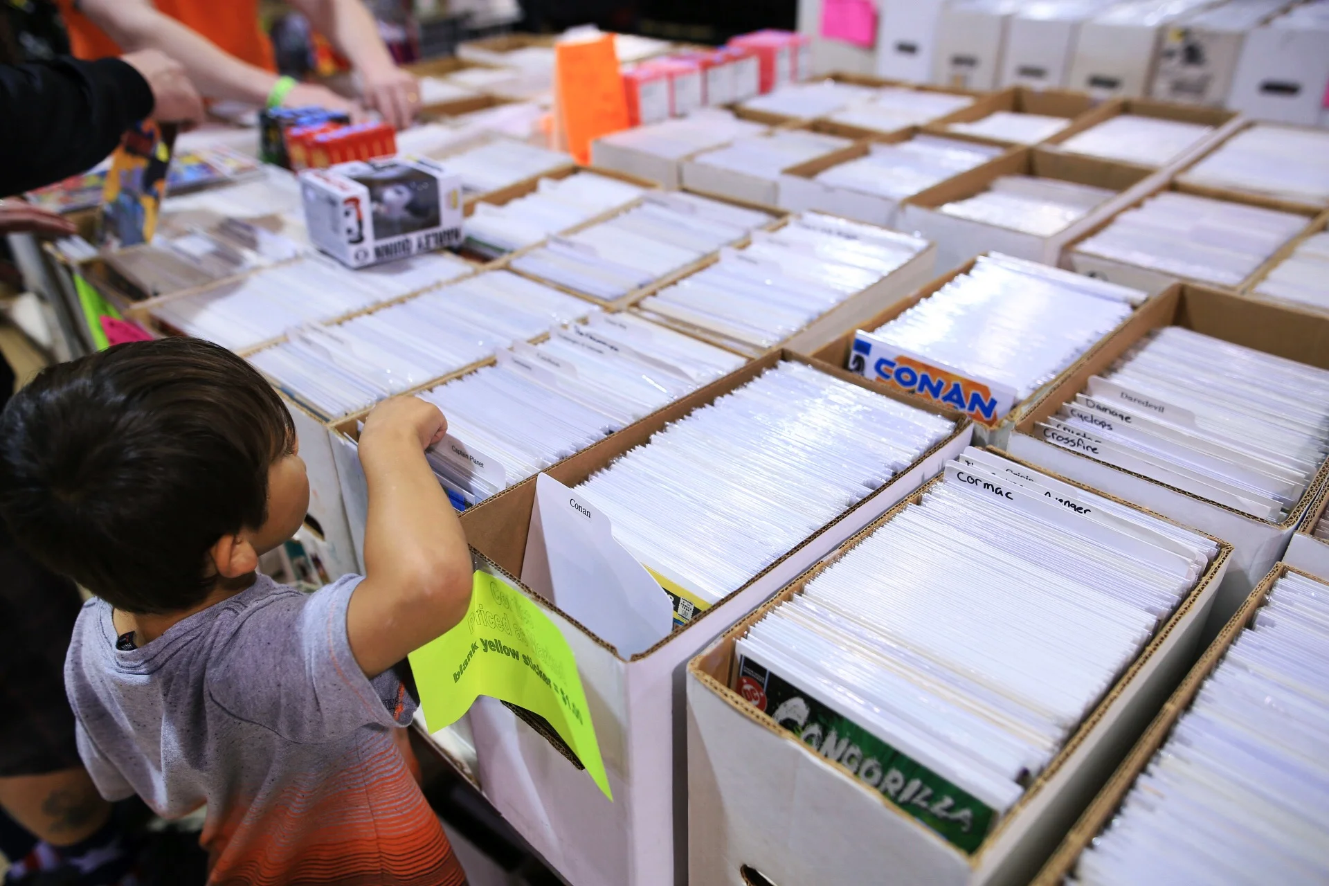  A kid, barely tall enough to see, peruses through collected comic books. 