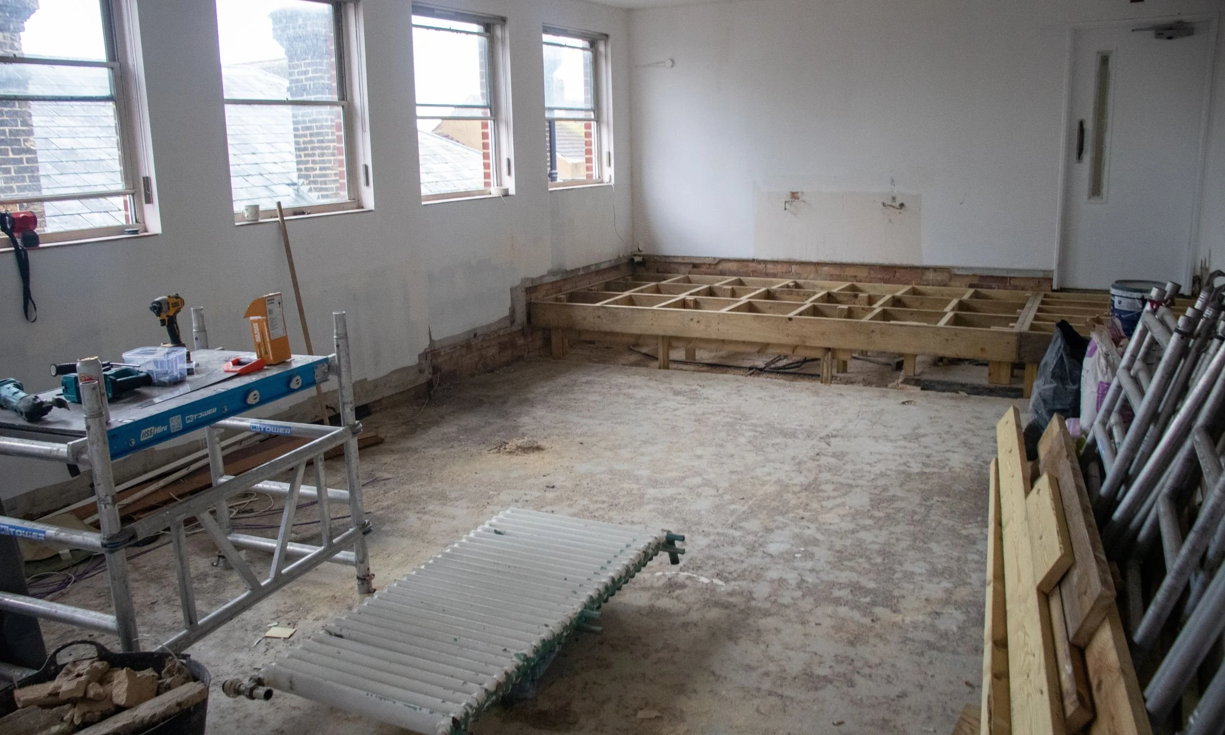 Room under renovation with wooden flooring framework, construction tools, and materials scattered around.