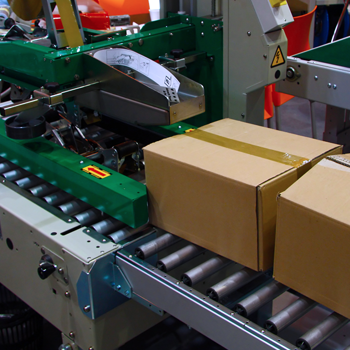 two cardboard boxes on conveyor attached to green case sealing machine