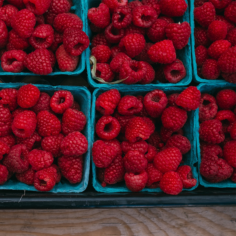 raspberries in blue fiber trays inside plastic flat on market shelf