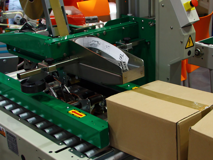 cardboard boxes being sealed with rubber adhesive tape on green case sealer