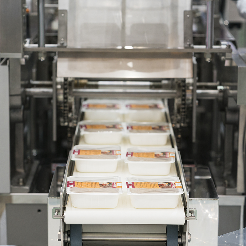 empty white trays with printed top seal film exiting outfeed conveyor of top seal machine