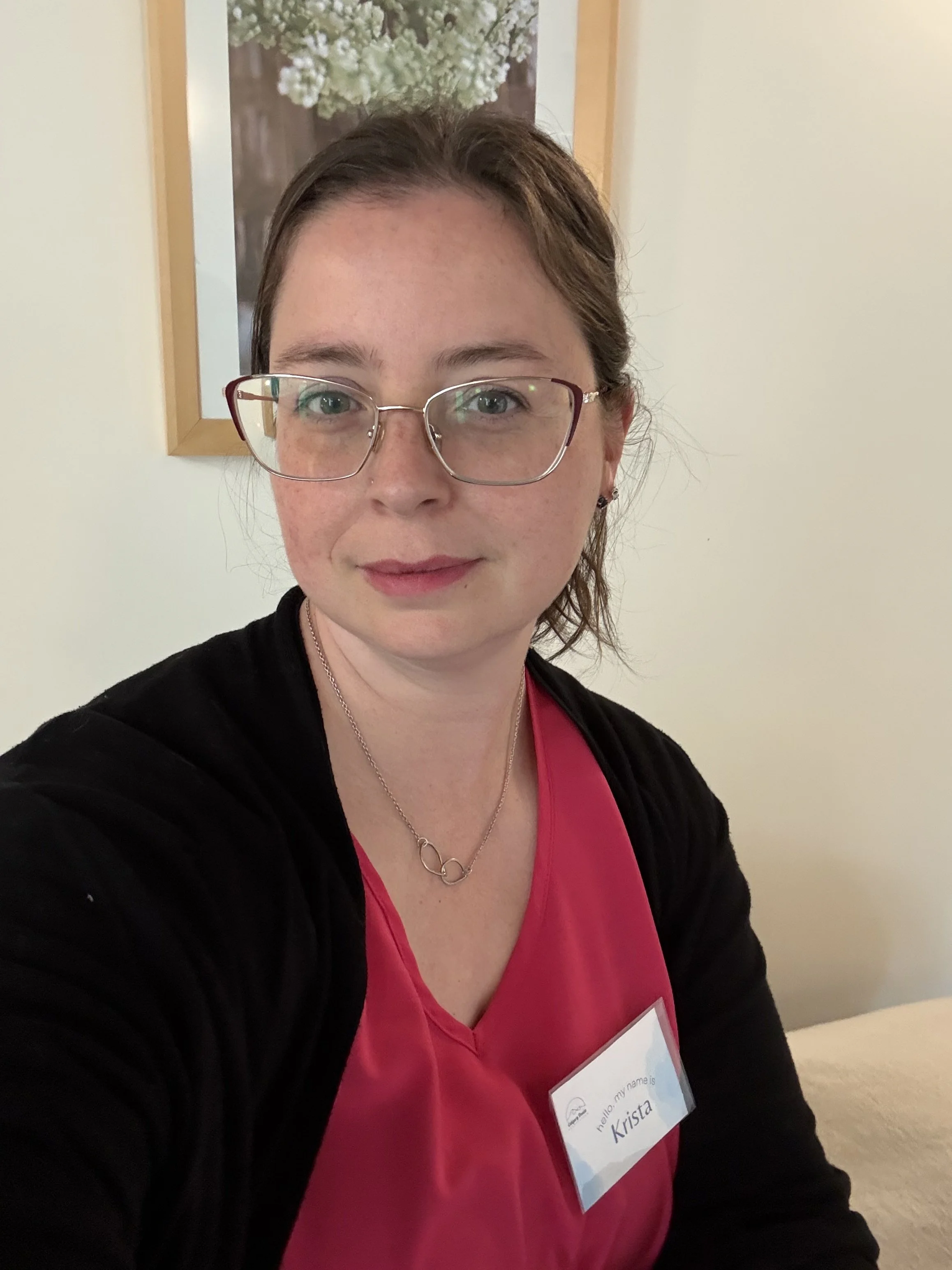 Woman smiling wearing glasses, a pink shirt, and black sweater.