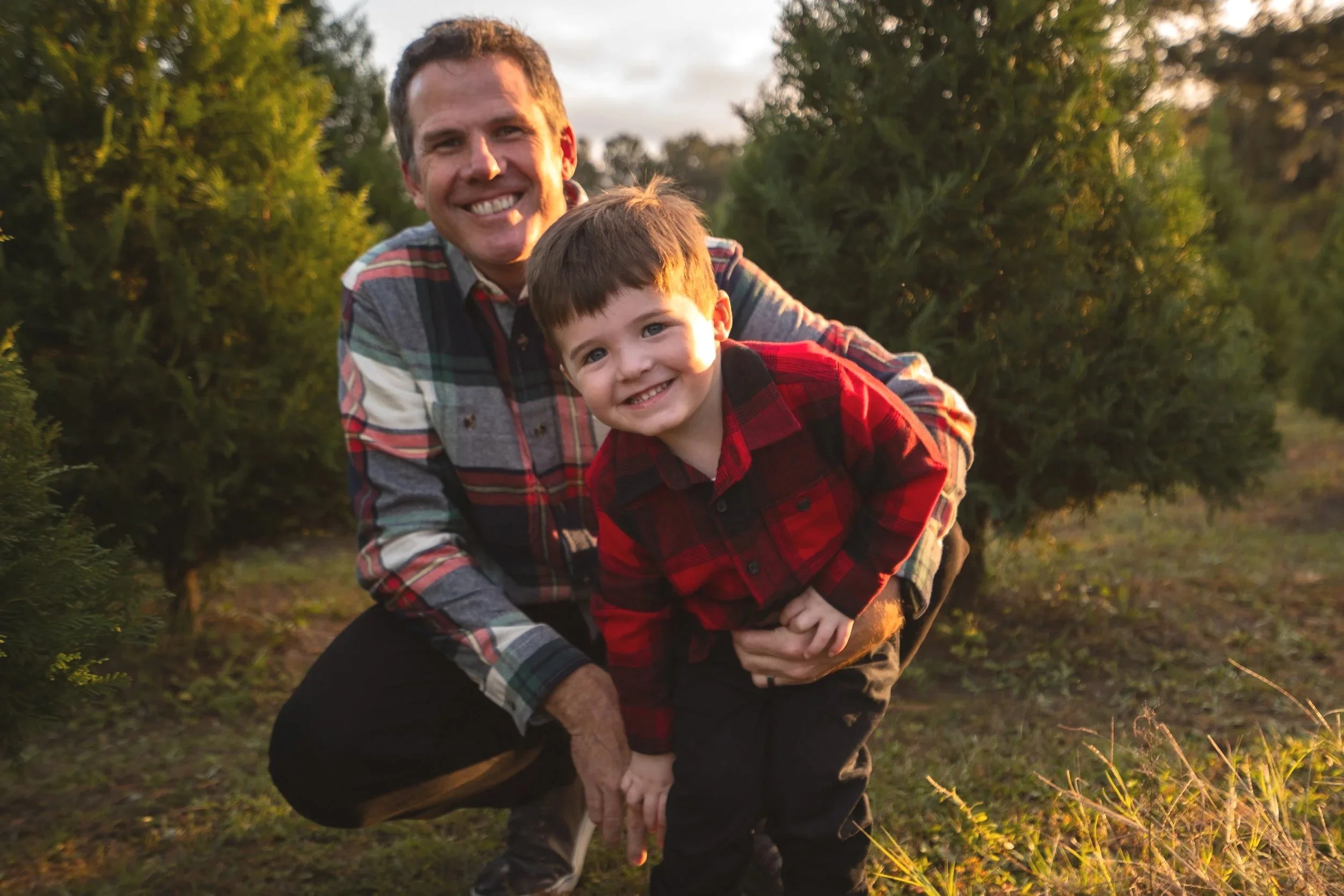 A Christmas tree farm mini session where dad and son are sharing sweet hug and while wearing red and black flannels