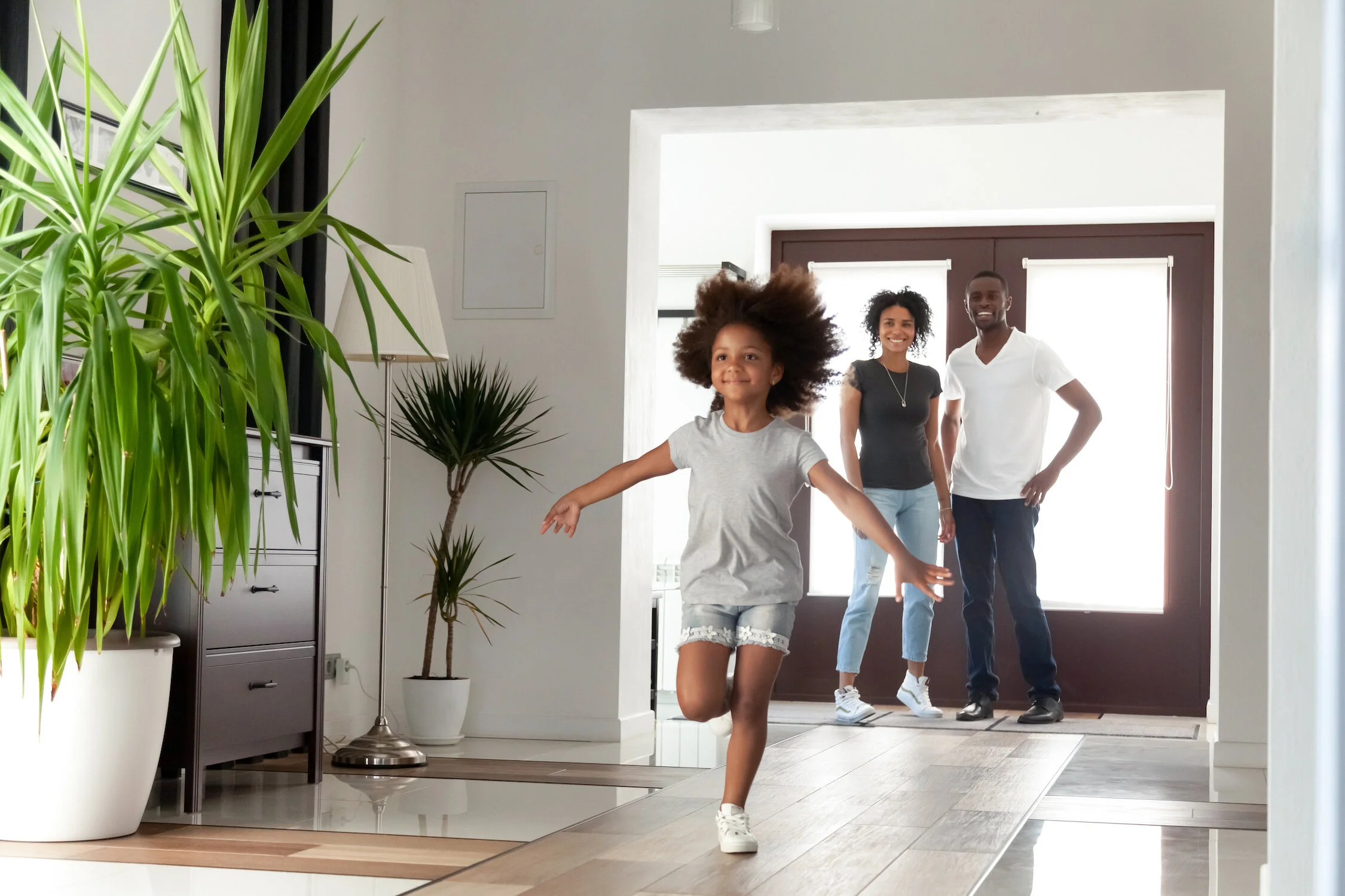 Excited little funny african girl running exploring big modern house on moving day