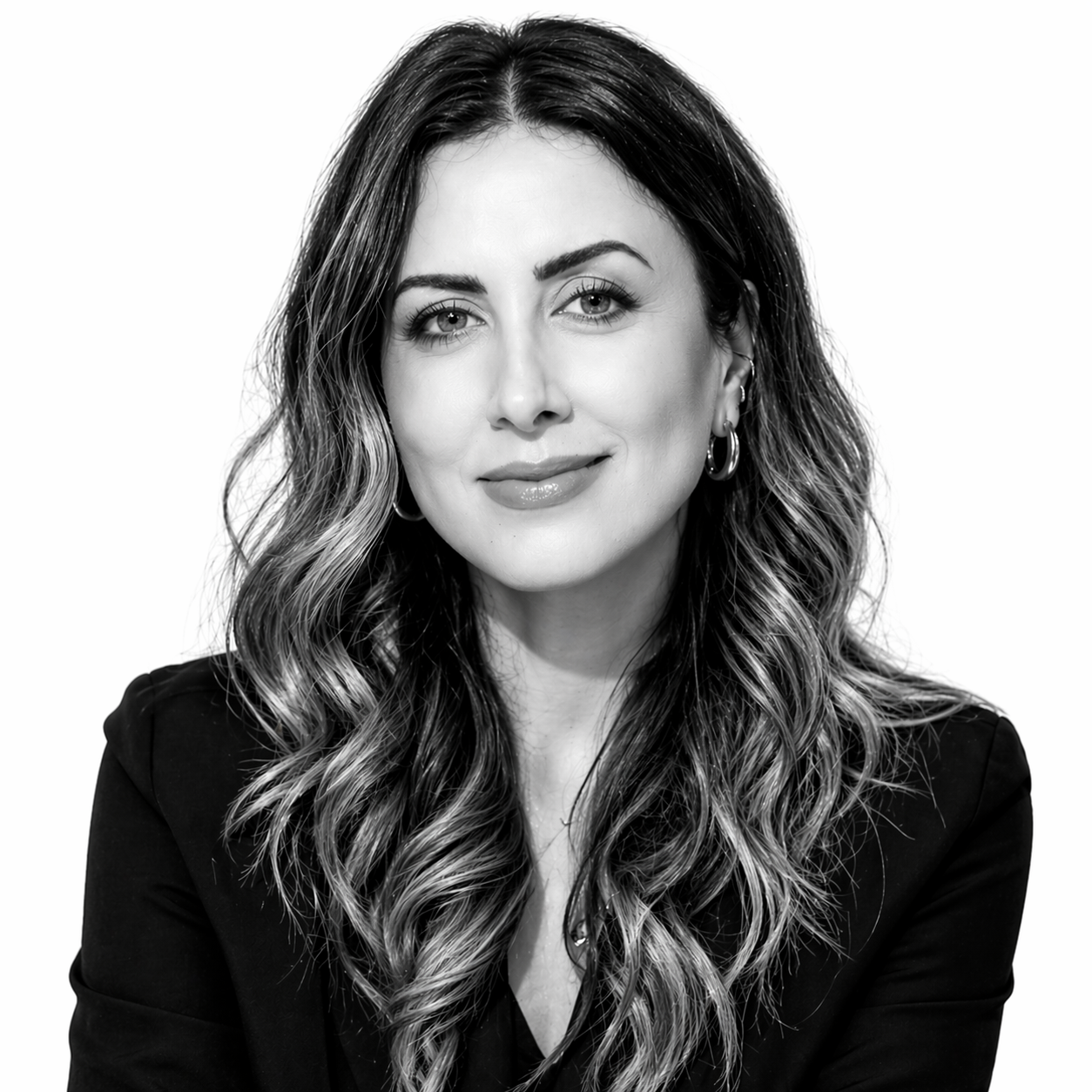 Black and white portrait of a woman with wavy hair, wearing hoop earrings and a dark blazer, smiling softly.