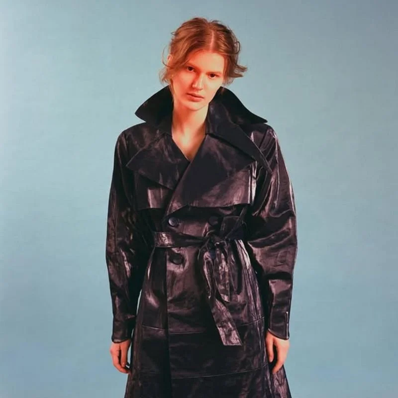 Model wearing a black trench coat against a blue backdrop