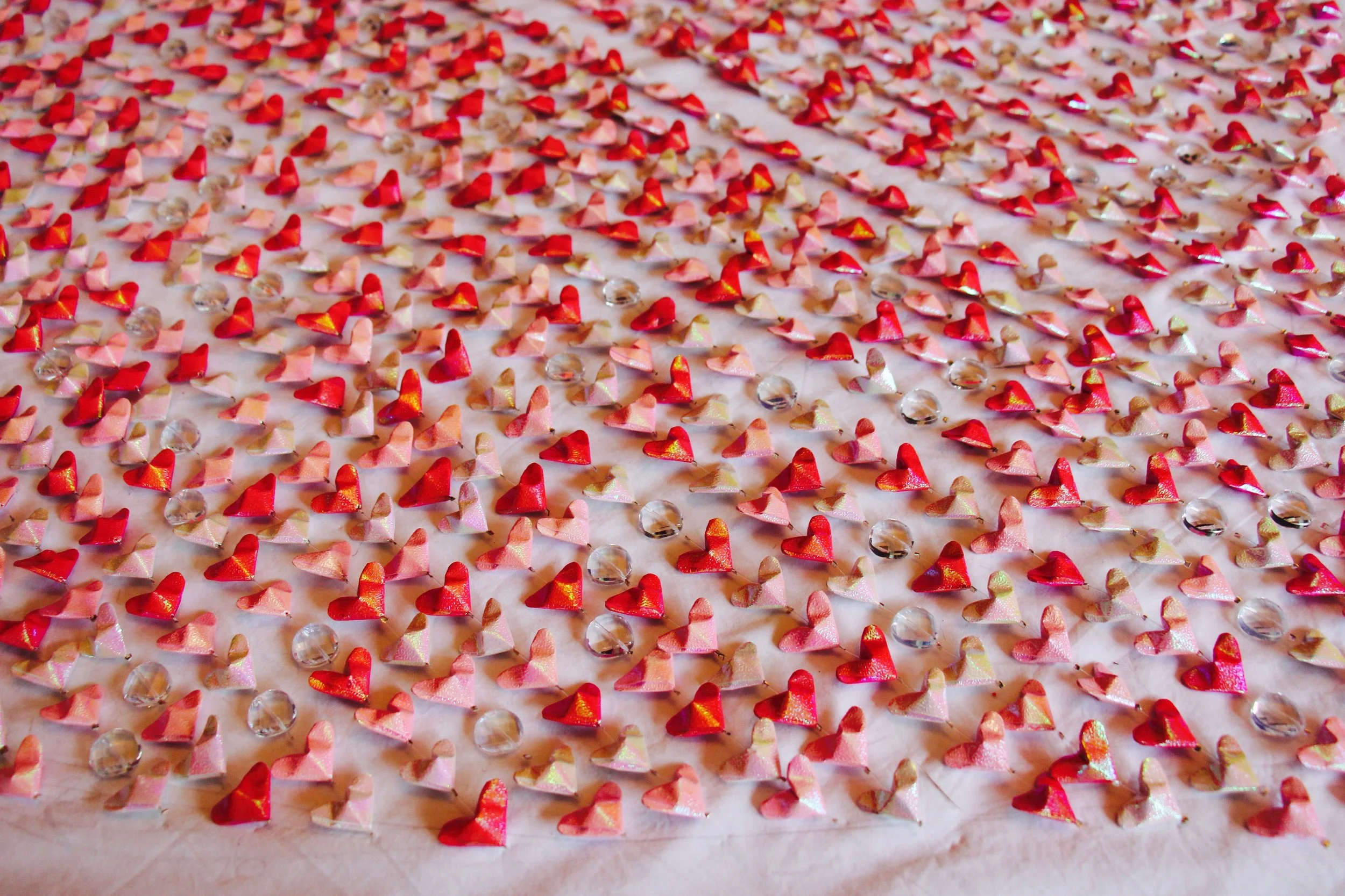 The series of lines of little origami hearts and crystals on the white cloth I use to plan my work.