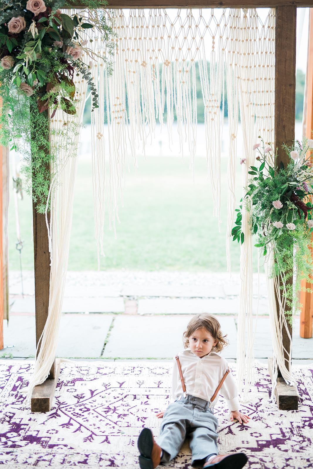 Wooden arch, asymmetrical floral, macrame, vintage rug and ring bearer all at the ceremony space - Pearl Weddings & Events