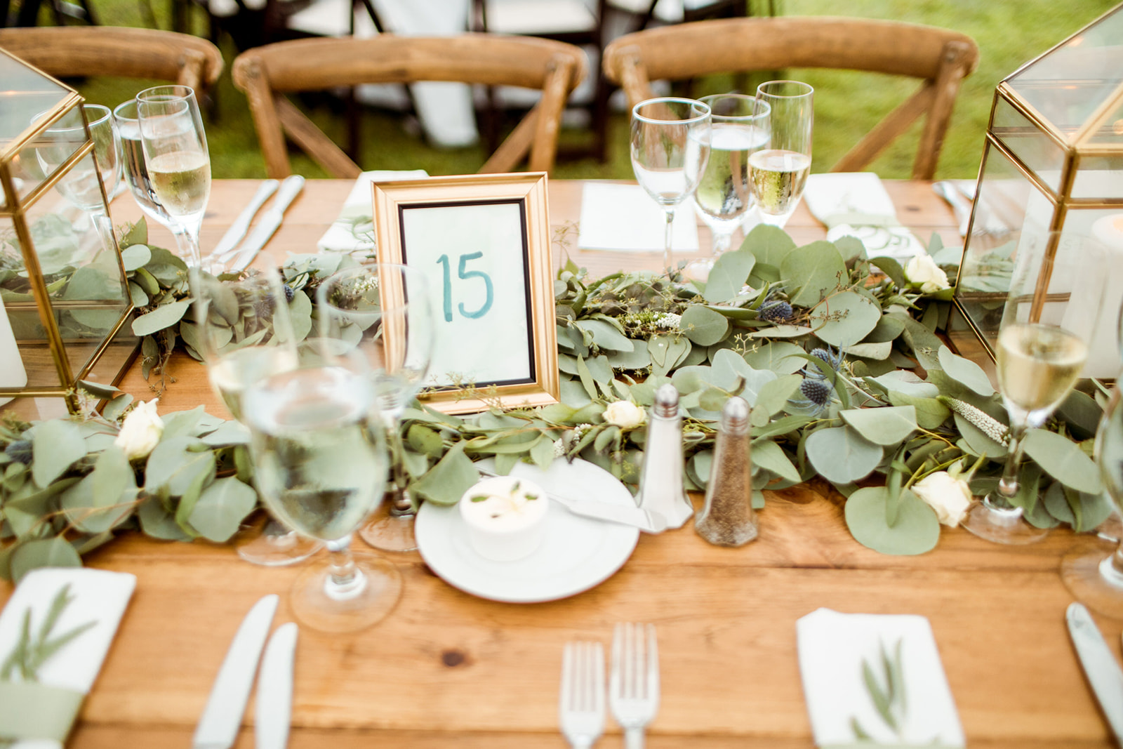 Lush greenery down the middle of the farm tables with framed table numbers and gold lanterns - Pearl Weddings & Events