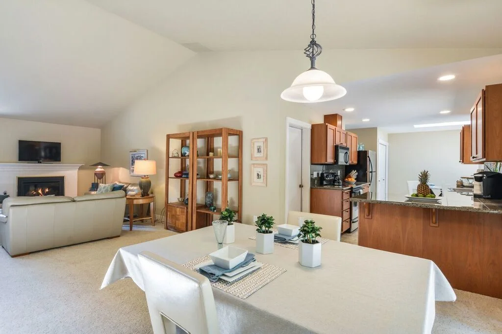 Living room, dining room, and kitchen flow together, but each has its own space under these high ceilings. Notice the door to the garage near the entrance to the kitchen.