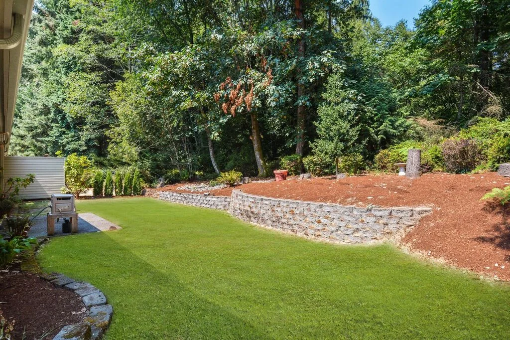 The back yard is bordered by maples, Douglas fir, cedar, alder, madrona, huckleberry bushes, and has a nice shape with the wall creating multiple levels.