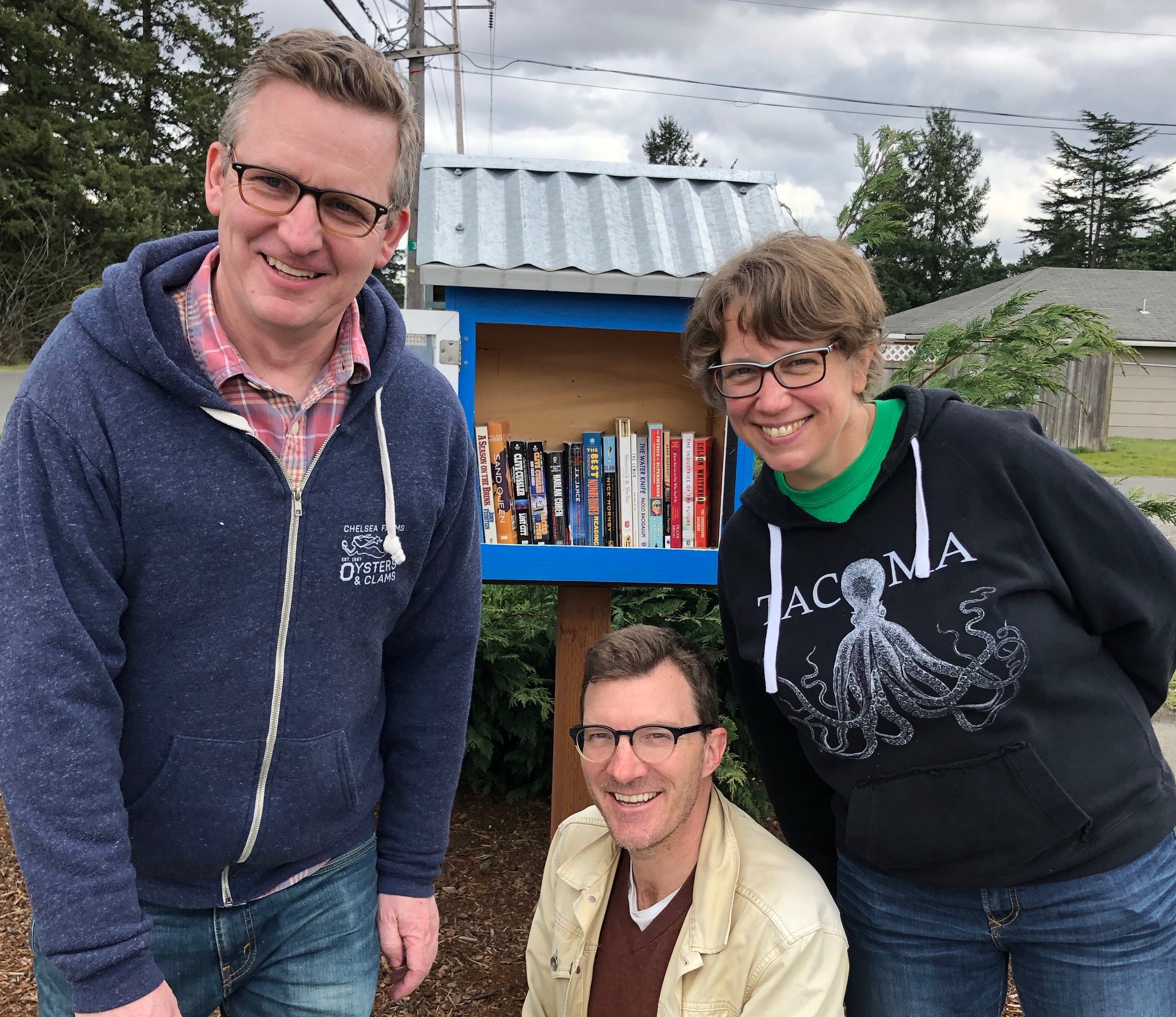 Meet Michelle Douglas of the Emergency Food Network crew and the Little Free Library they host in a diverse Lakewood neighborhood. Pictured with Michelle are Patrick Moreland and Steve Cathersal who come home to Tacoma to volunteer at the Emergency Food Network with Dr. Jamie!