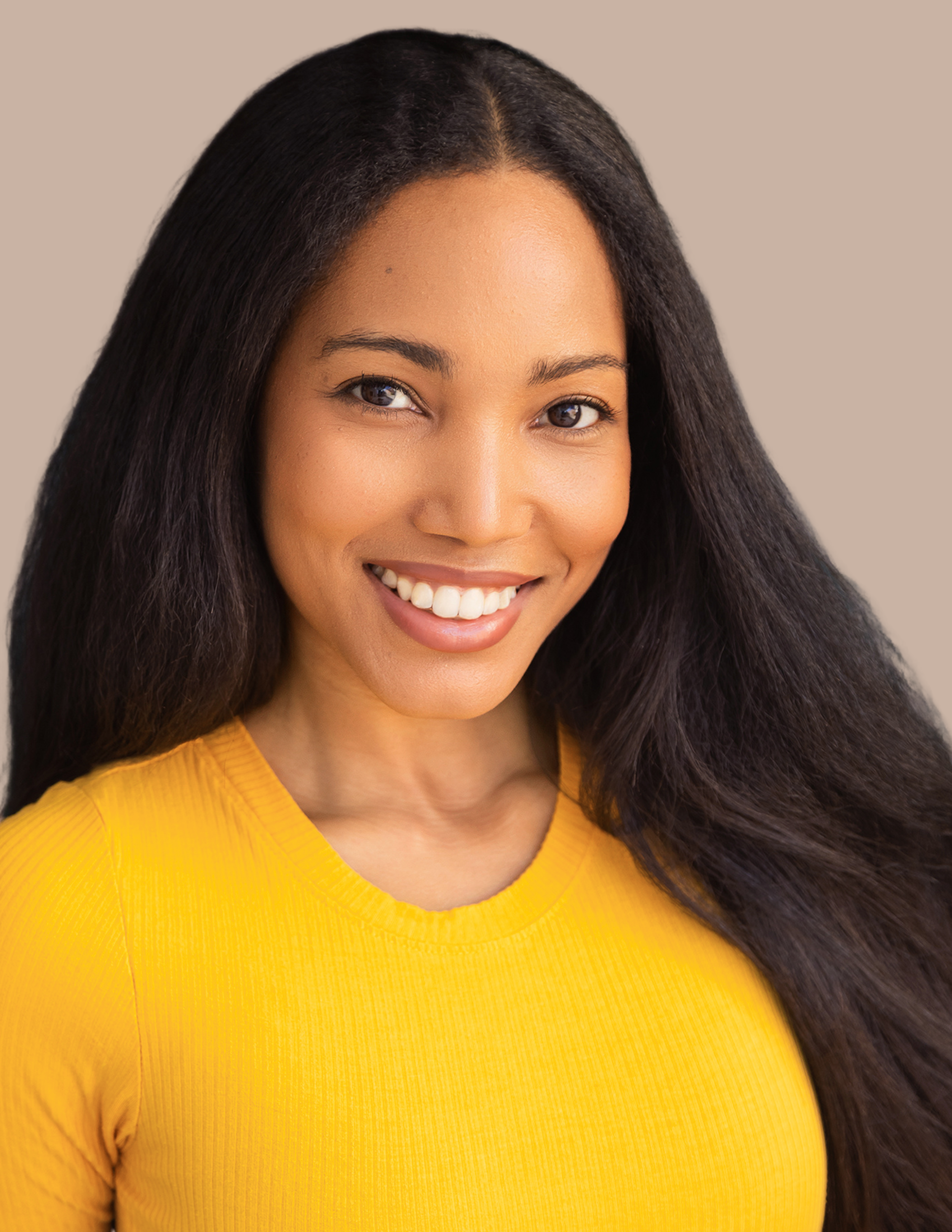 Close-up of a smiling woman with long dark hair, wearing a bright yellow top, against a neutral background.