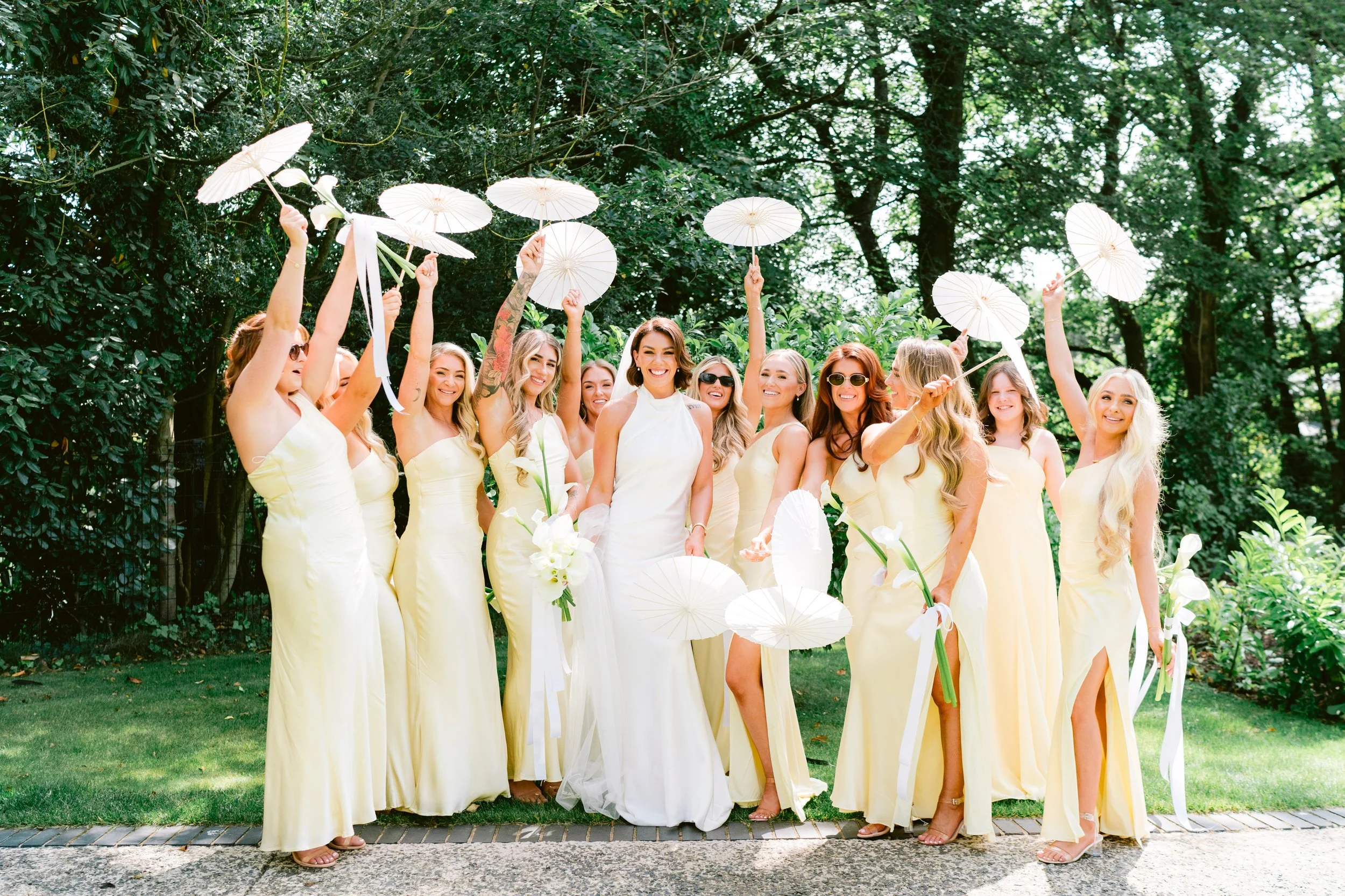 bride on her wedding day surrounded by bridesmaids in yellow dresses holding white parasols