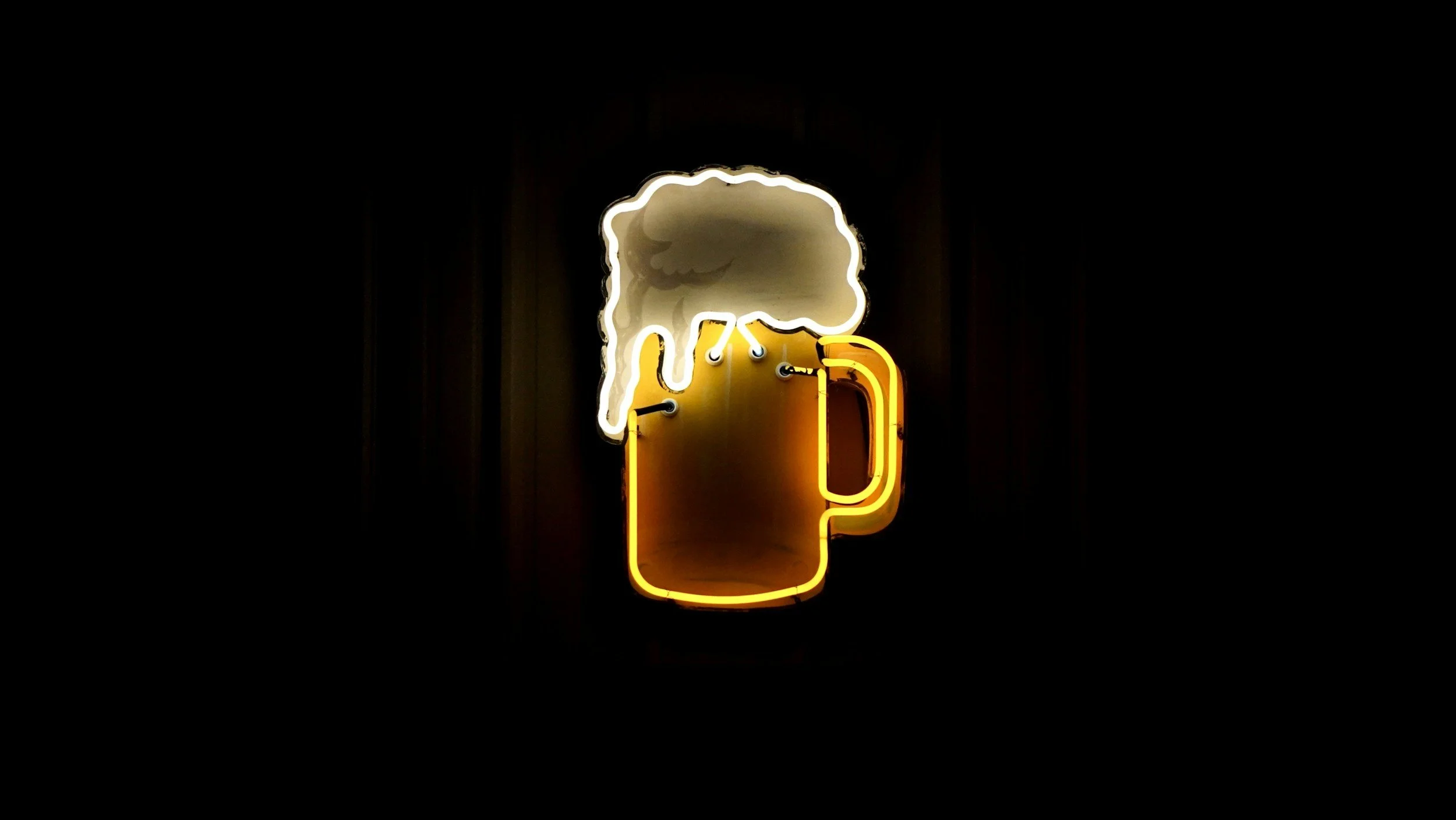 Neon sign of a beer mug with foam on top, outlined in yellow and white lights, against a black background.