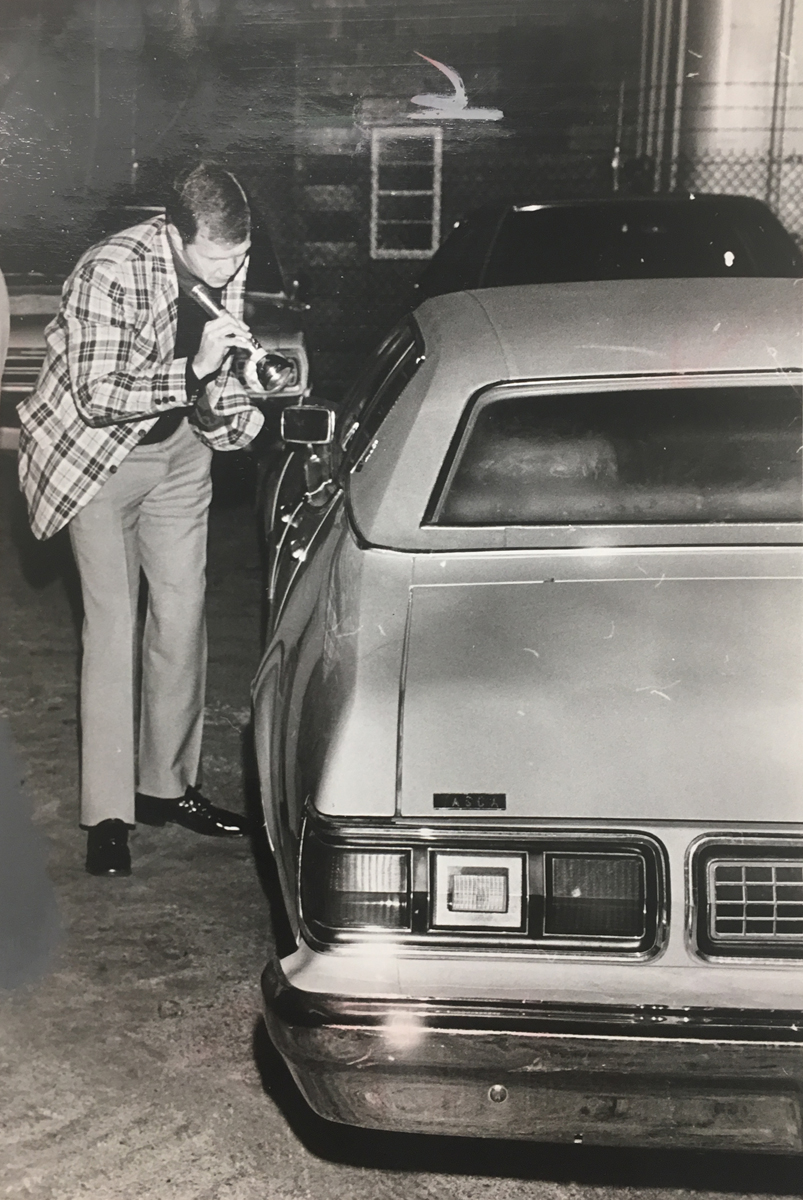 Another policeman shines a flashlight into the Mercury where George Basmajian was murdered. Courtesy of the Providence Journal/William K. Daby.