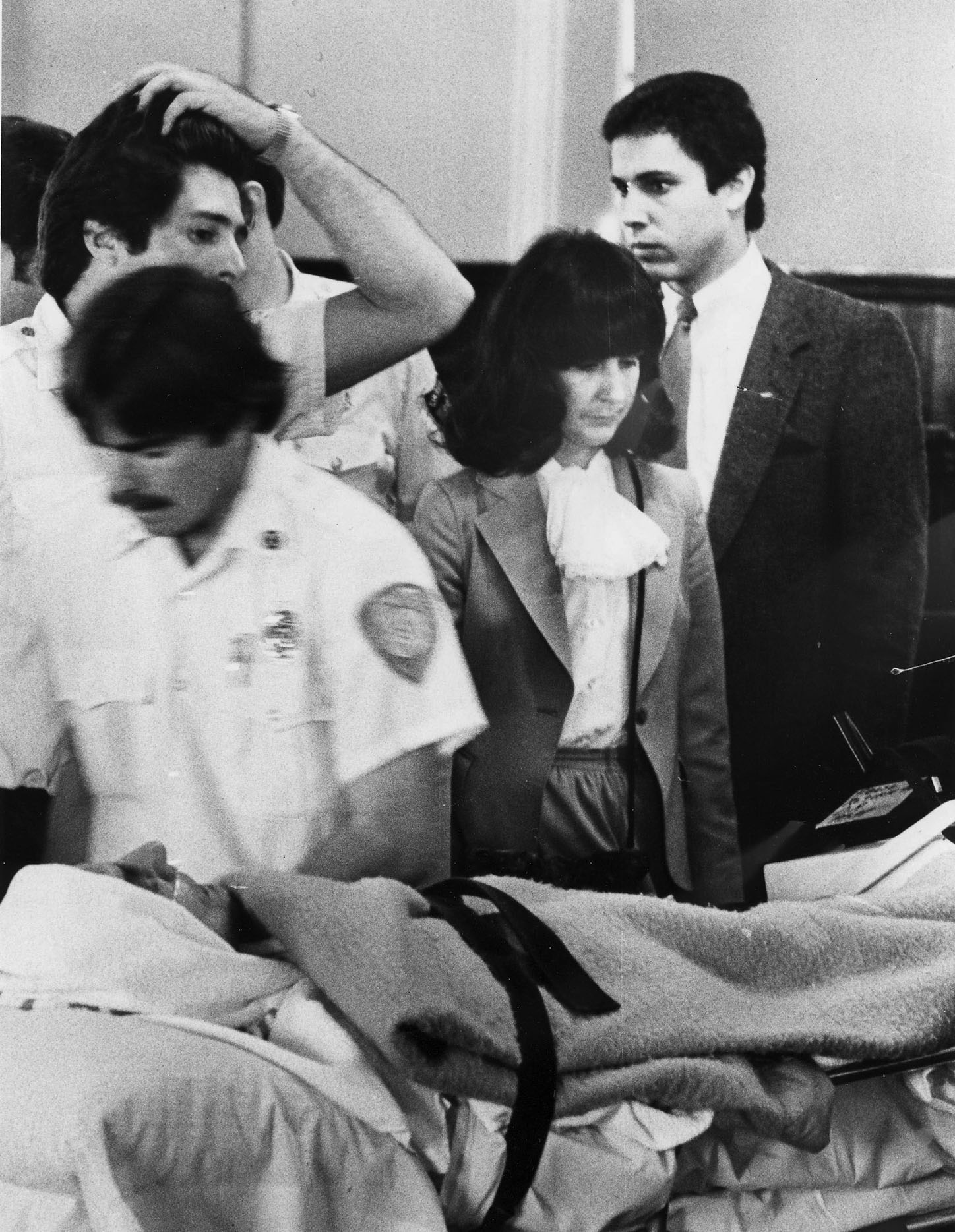 A pale Raymond Patriarca, swathed in sheets and carried on a stretcher, is accompanied by Dr. Barbara Roberts and other medical personnel at his arraignment in March 1981. Courtesy of The Providence Journal.