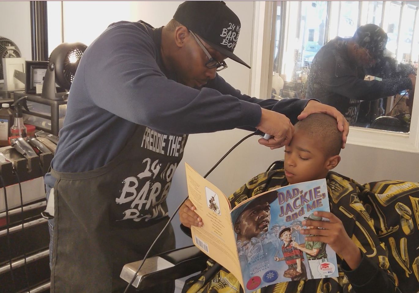 Real Dads Read Barbershop partner Freddie Johnson, III reading with Kenneth Braswell Jr. at Anytime Cutz in Atlanta.