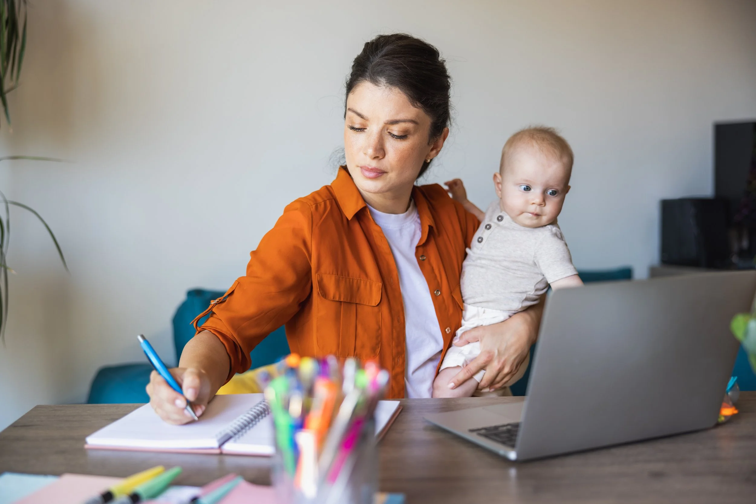 Professional woman writing in a notebook while working on her laptop