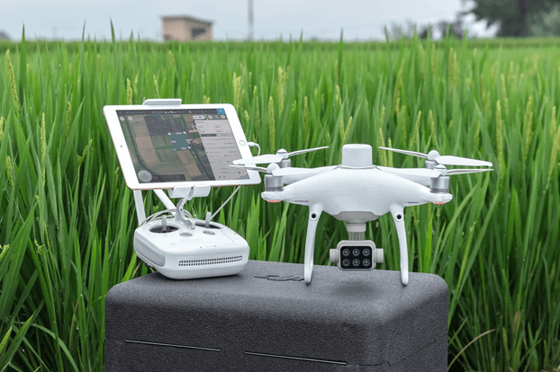 Dron blanco y control remoto con tableta en un campo de cultivo.