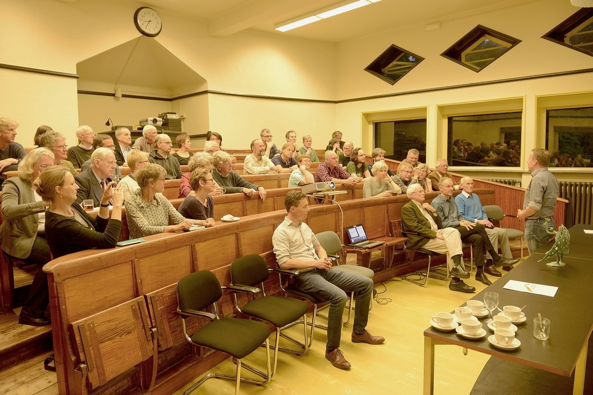Leden en bestuur van vereniging Mooi Wageningen. Met beeld van Gelderse Pauwenveer op de vergadertafel en voorzitter Patrick Jansen aan het woord (Lustrum 2017)
