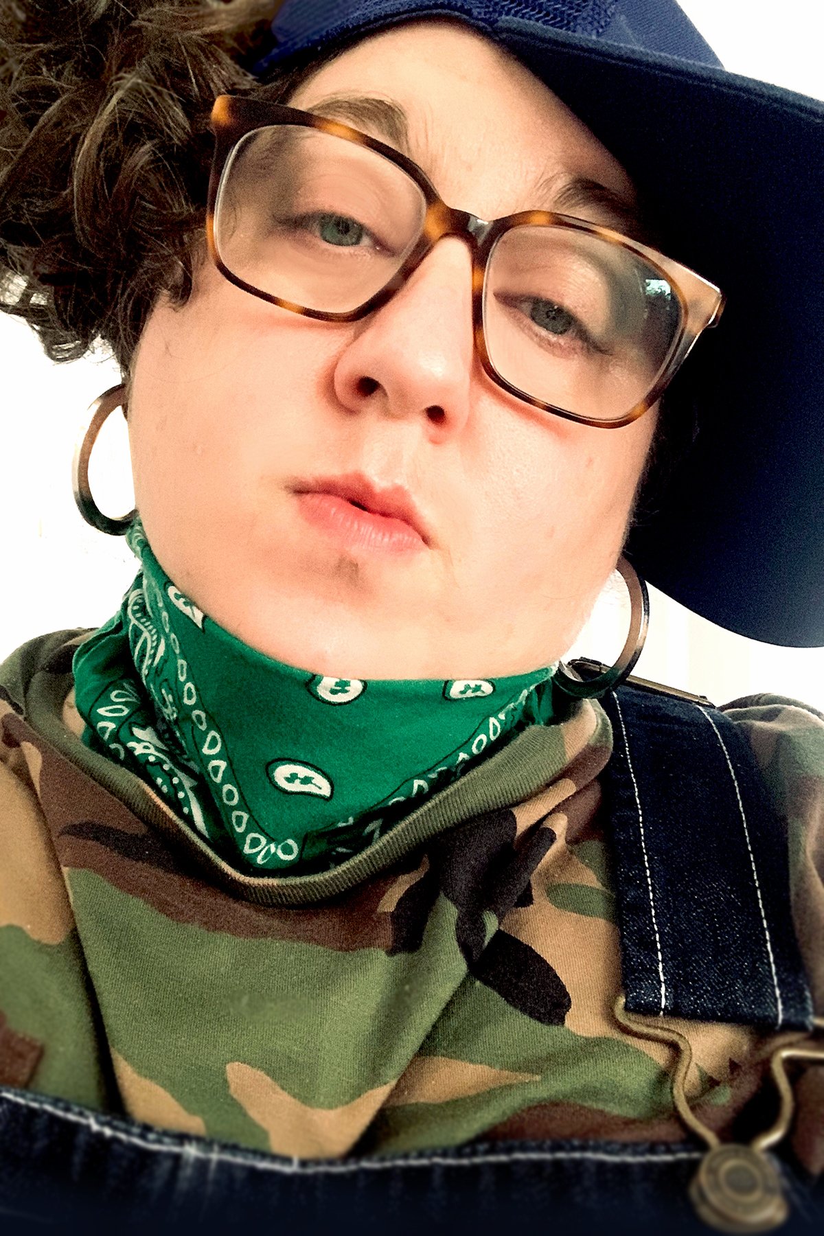  [A bio picture of the artist, Constantina Zavitsanos, depicts them in overalls, camo, hoops and paisley with white skin and dark, curly, hair—half tucked under a hat.]  Photo credit: Allison Harris 
