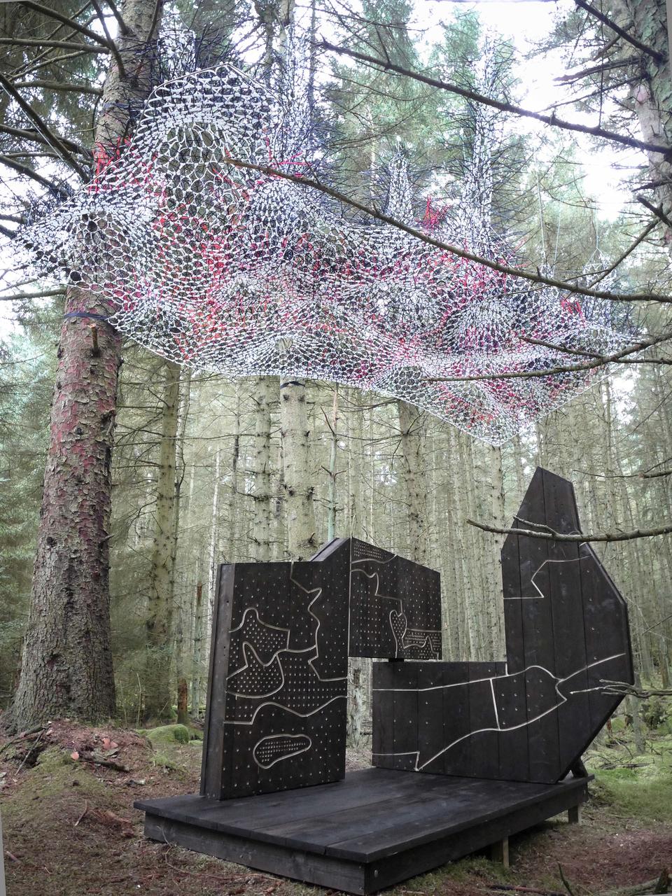 On the ground, a charred-timber performance space frames a stunning view into the heart of Smugglers Rigg. Overhead, suspended amongst the overhanging branches, is a semi-transparent form created from 15,000 woven cable ties. The structure and contours of each aspect of the piece relate to the different ages of the trees in the surrounding area, creating two abstracted maps of the Kielder forest canopy.