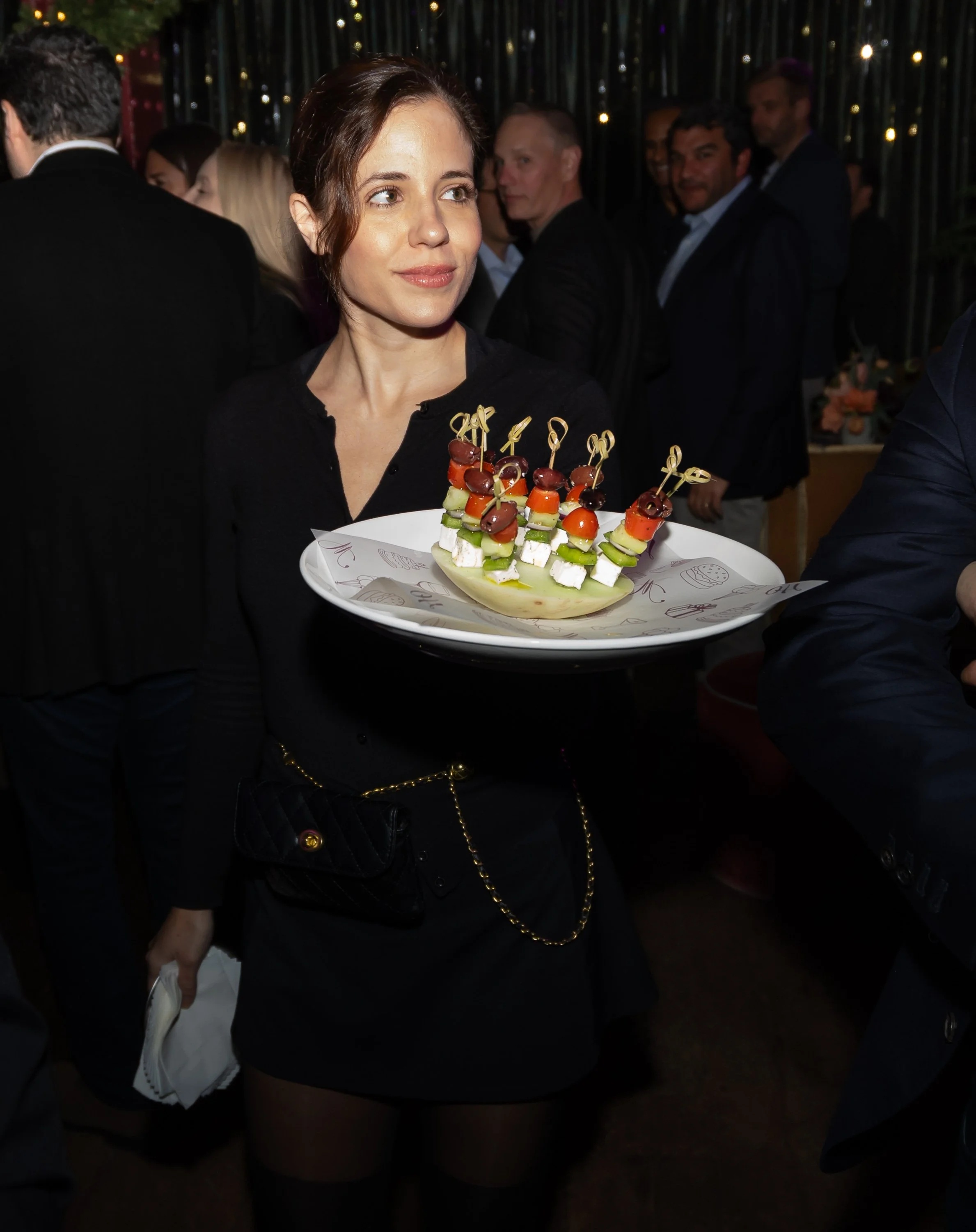 A woman holding a tray of Mediterranean-style appetizers at a social event or party.