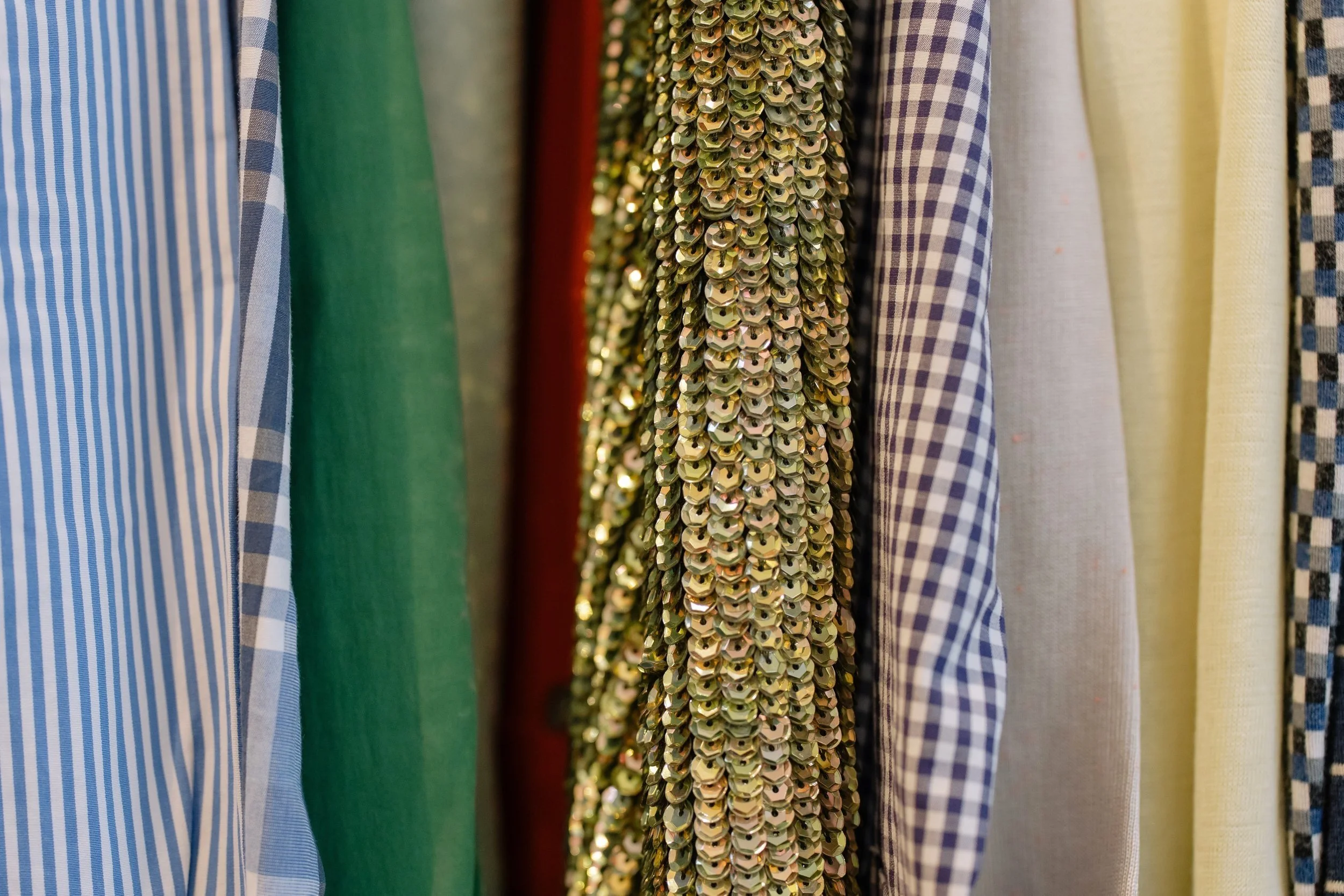 a close up on a row of ordinary clothing in a closet, with a sparkly sequin jacket in the middle