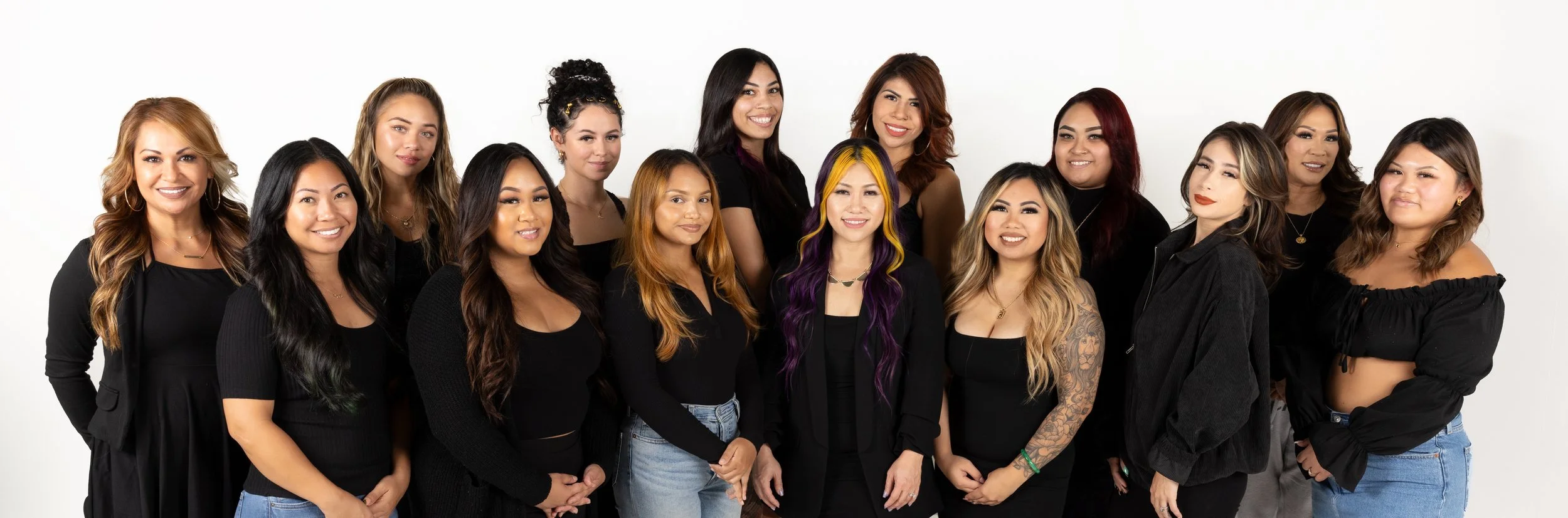 Group of diverse women posing together against a white background, wearing black and casual clothing.