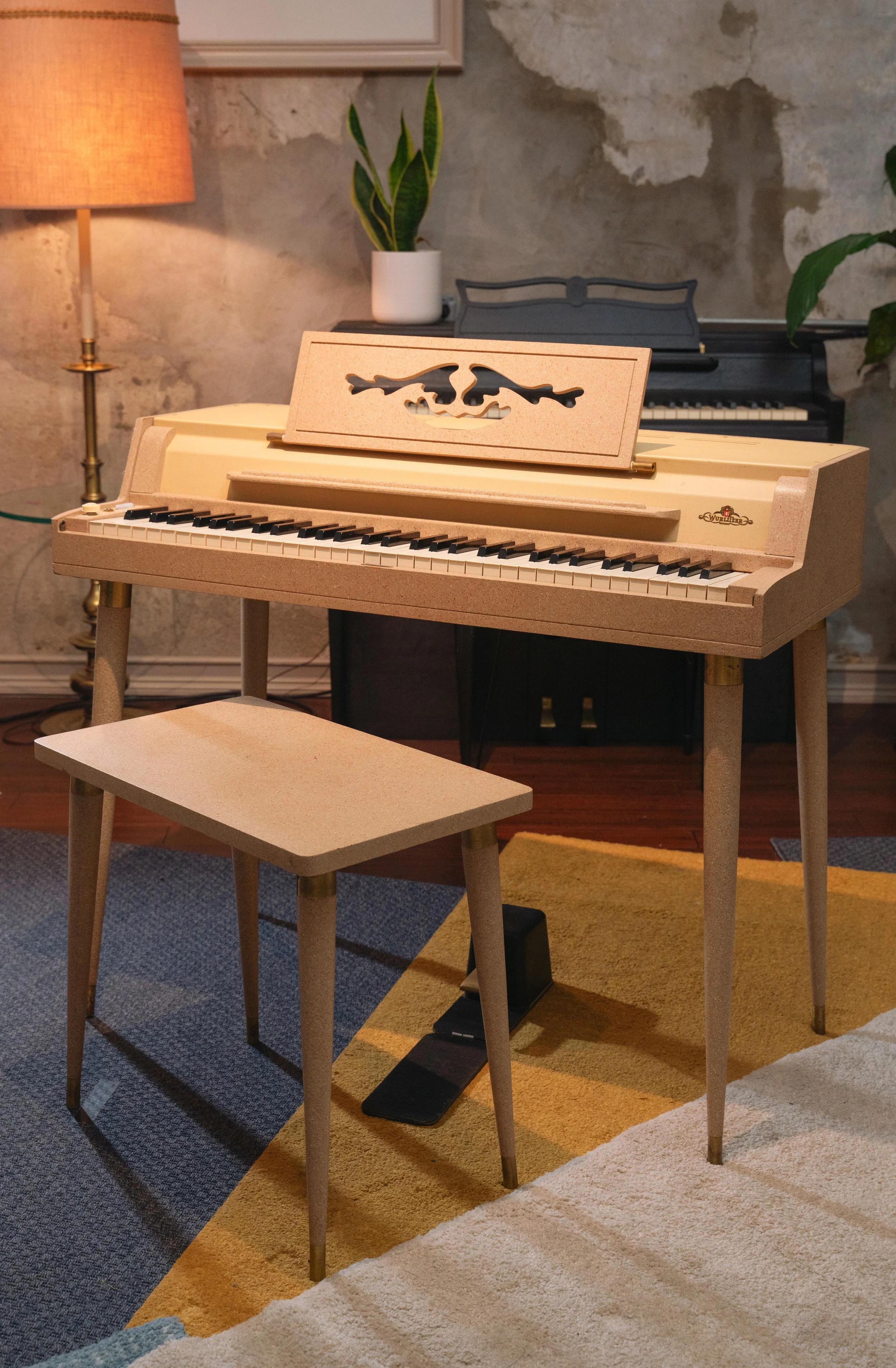 A Wurlitzer 120 on three carpets that are blue, yellow, and beige, with a Wurlitzer 700 in the background against a concrete wall.