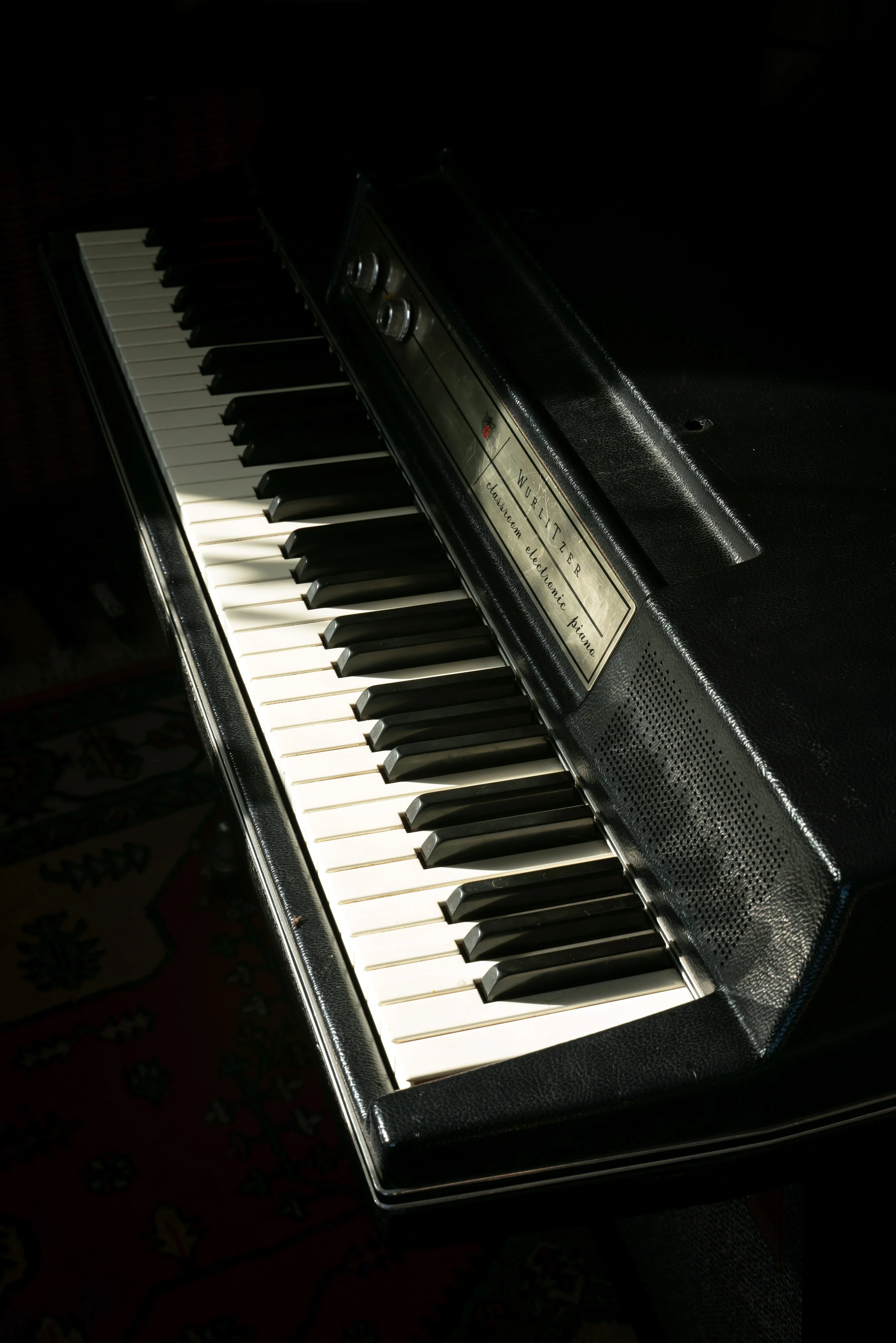 A Wurlitzer 214 in black from a dramatic angle with shadows and direct sunlight across some of the keys.