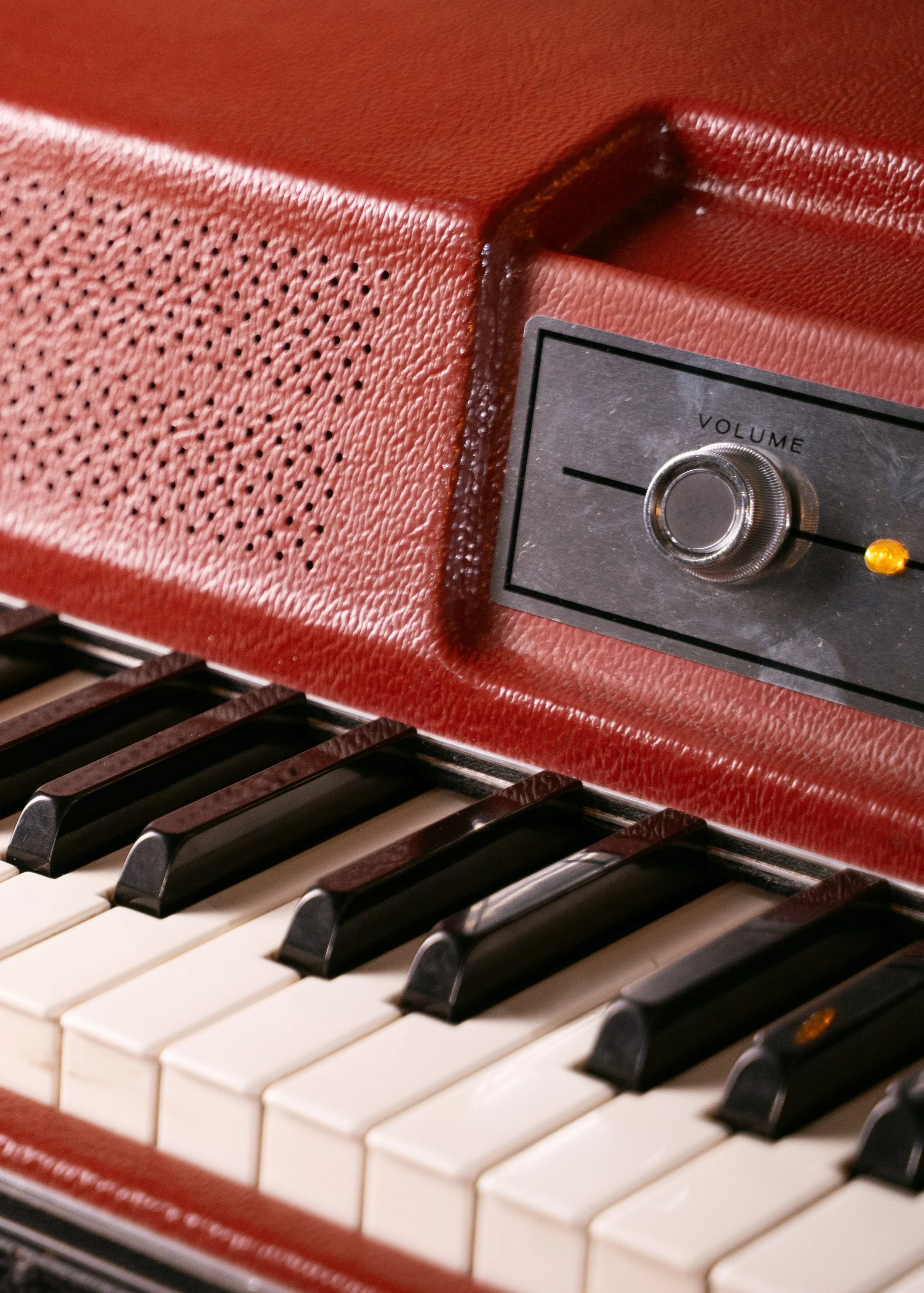 A closeup of a Wurlitzer 200 with a red lid showing the volume knob and some of the middle register keys.