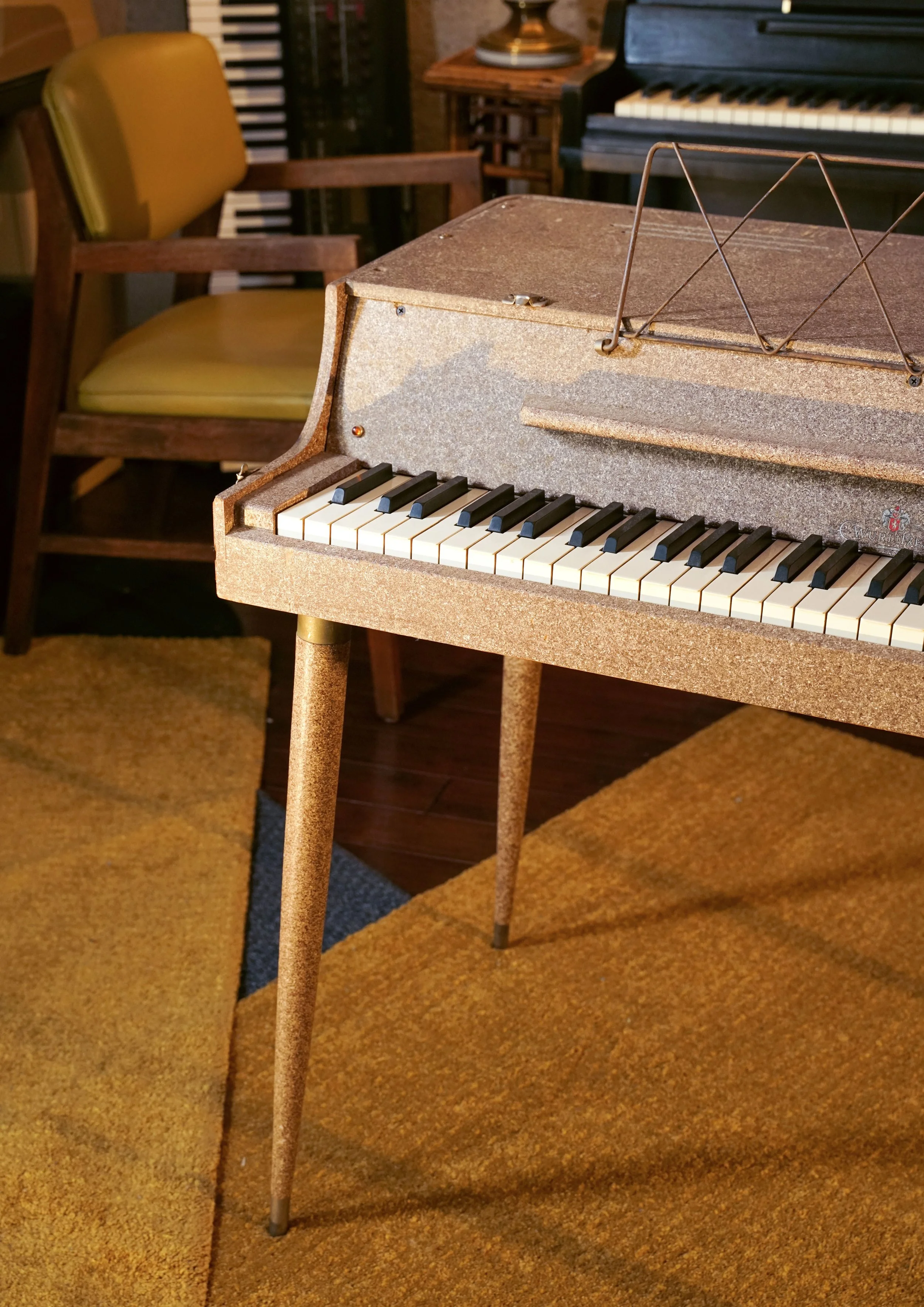 A Wurlitzer 112 shown in a room with orange carpet and a yellow midcentury chair in the background.