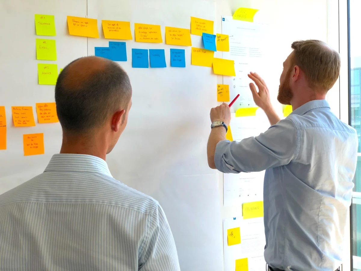 Male Project Manager Organizing Sticky Notes in Front of Fellow Male Software Developer