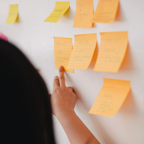 Person Pointing at Wall of Sticky Notes