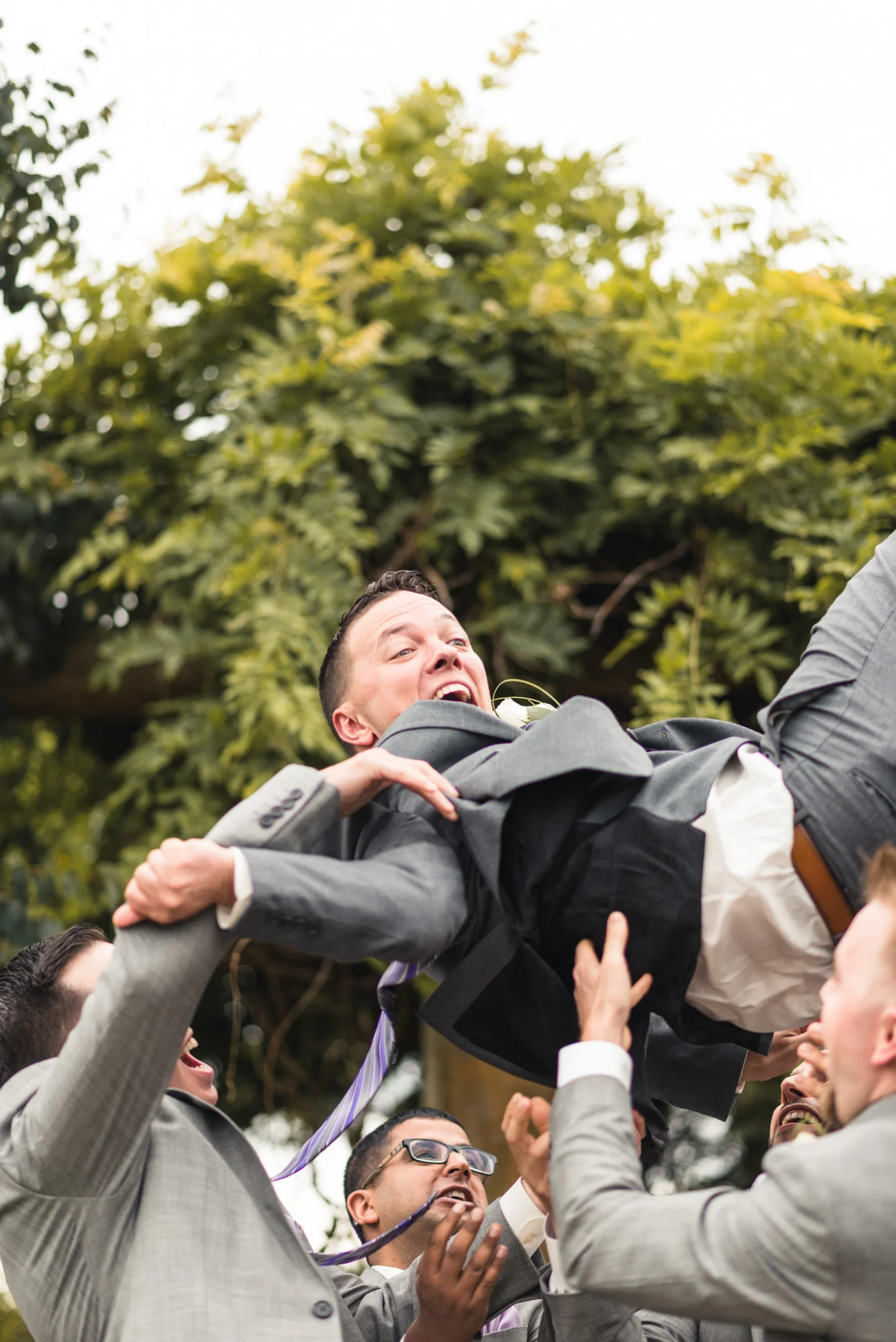 Groomsmen tossing Groom into air