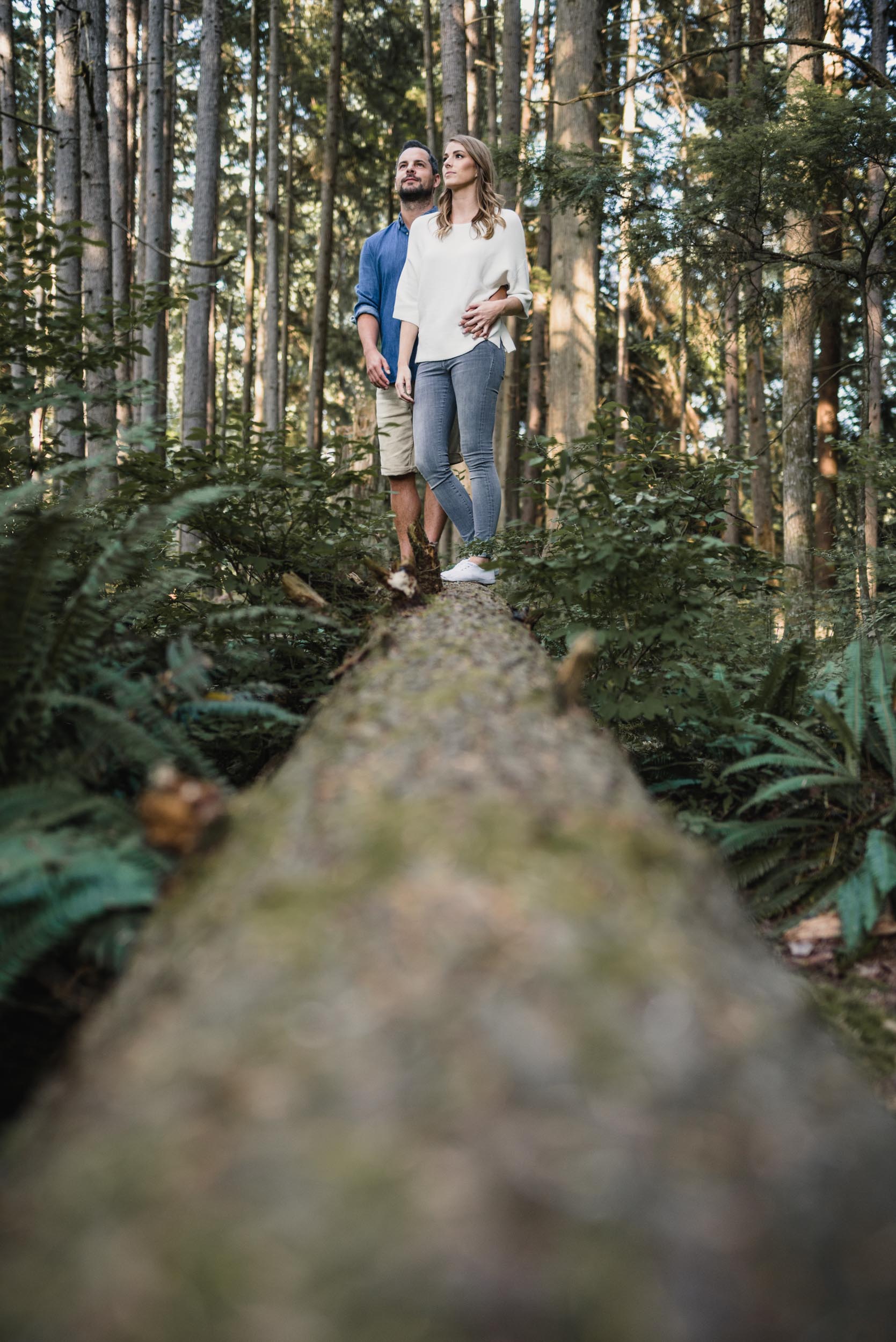 Couple stands together on fallen tree in forest